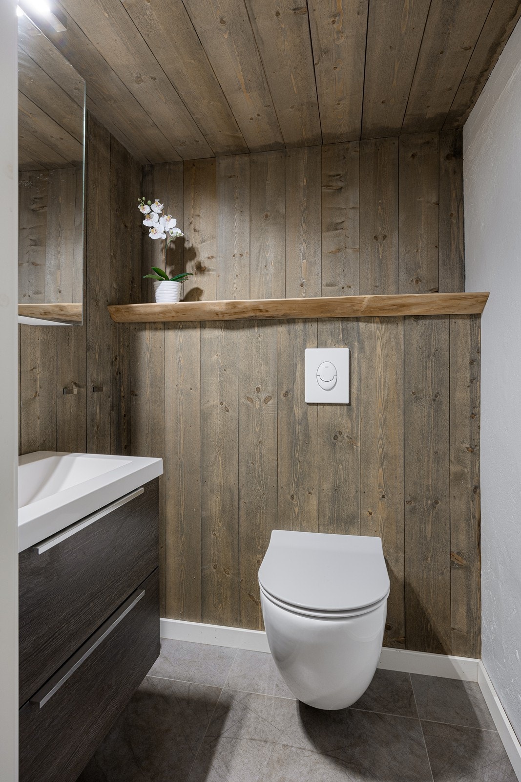 Wc-rom i kjelleretasjen med fliser på gulvet, lune panelvegger, servantinnredning og veggmontert toalett Galleribilde