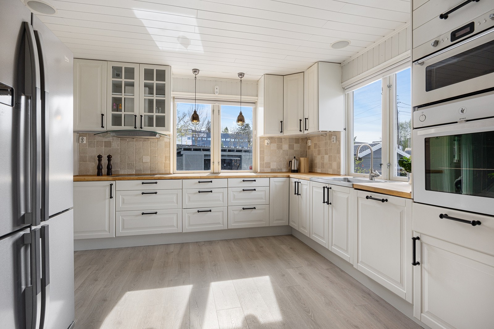 Kjøkkenet er pent innredet med stilren, takhøy innredning, enstavs gulv og lysmalte panelvegger Galleribilde