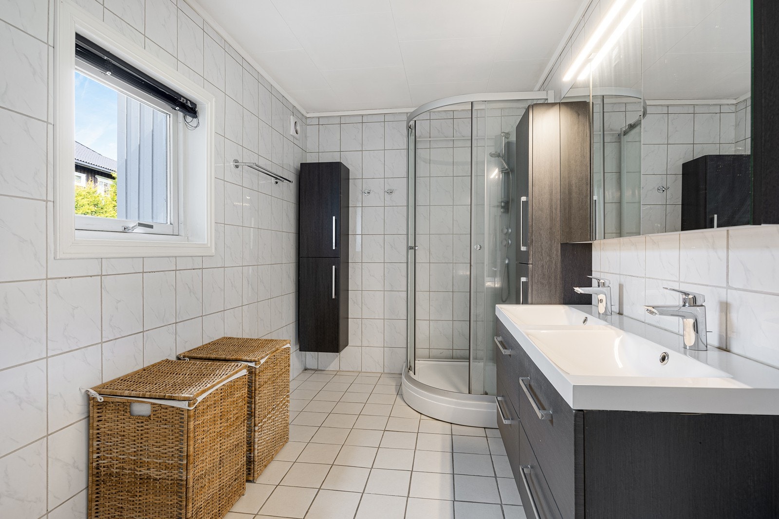 Badet første etasje har lyse fliser på gulv og vegger, gulvvarme, dusjkabinett og et gulvmontert toalett Galleribilde