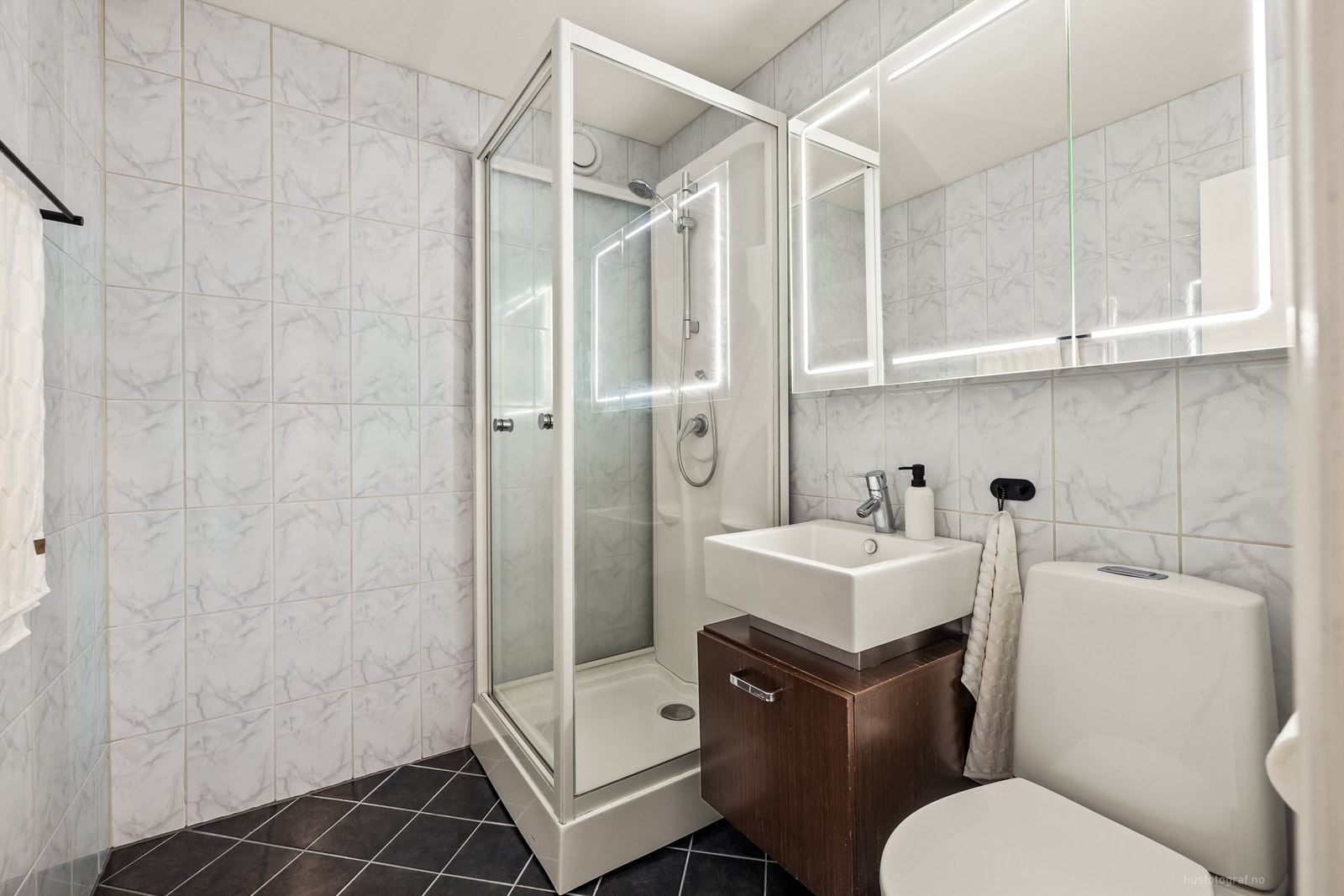 Badet er innredet med vegghengt servantinnredning, dusjkabinett, gulvstående toalett og speilskap med lys Galleribilde