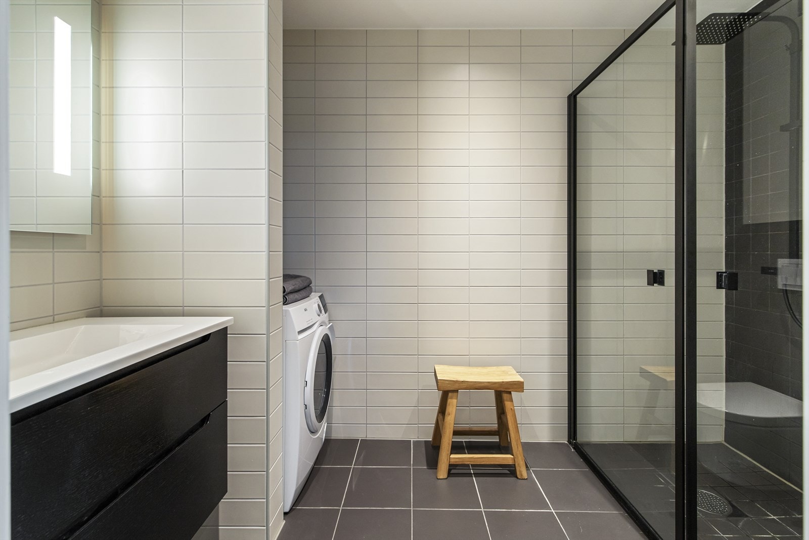 Rommet er innredet med servant nedfelt i baderomsinnredning med skuffeseksjoner, speil med belysning, vegghengt toalett samt dusjsone med regnfallsdusj og innfellbare glassvegger. Det er opplegg for vaskemaskin. Galleribilde