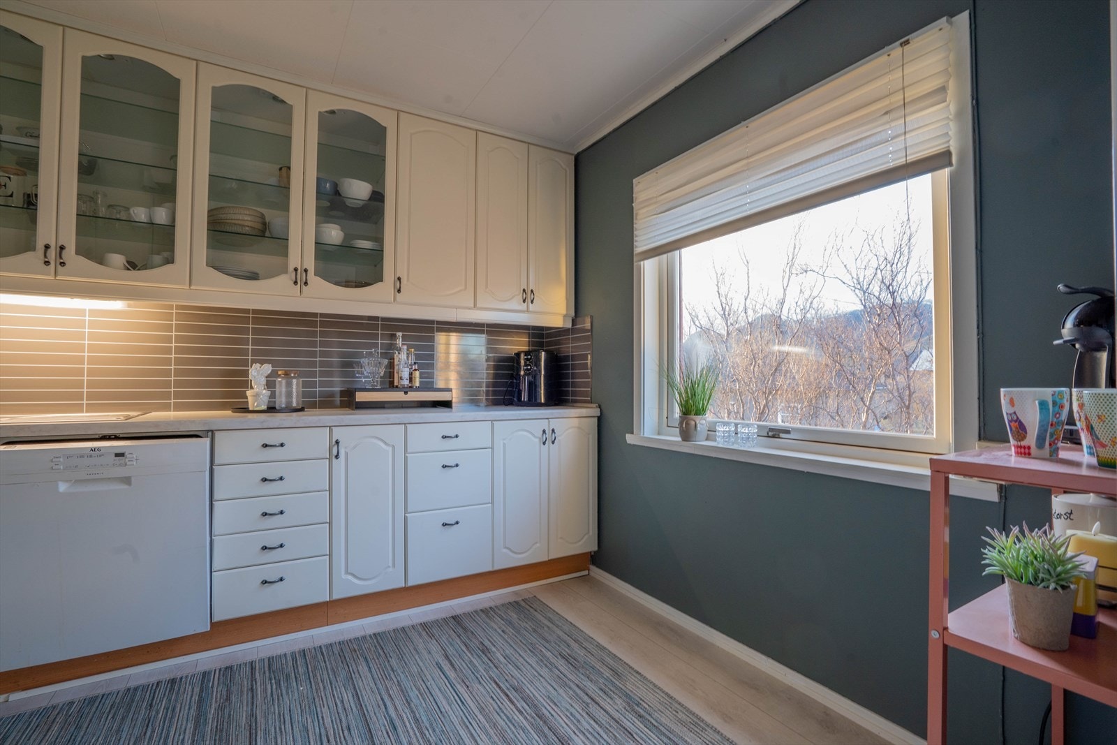 Lyst kjøkken med stort vindu som slipper inn naturlig lys og gir utsikt mot nabolaget. Galleribilde