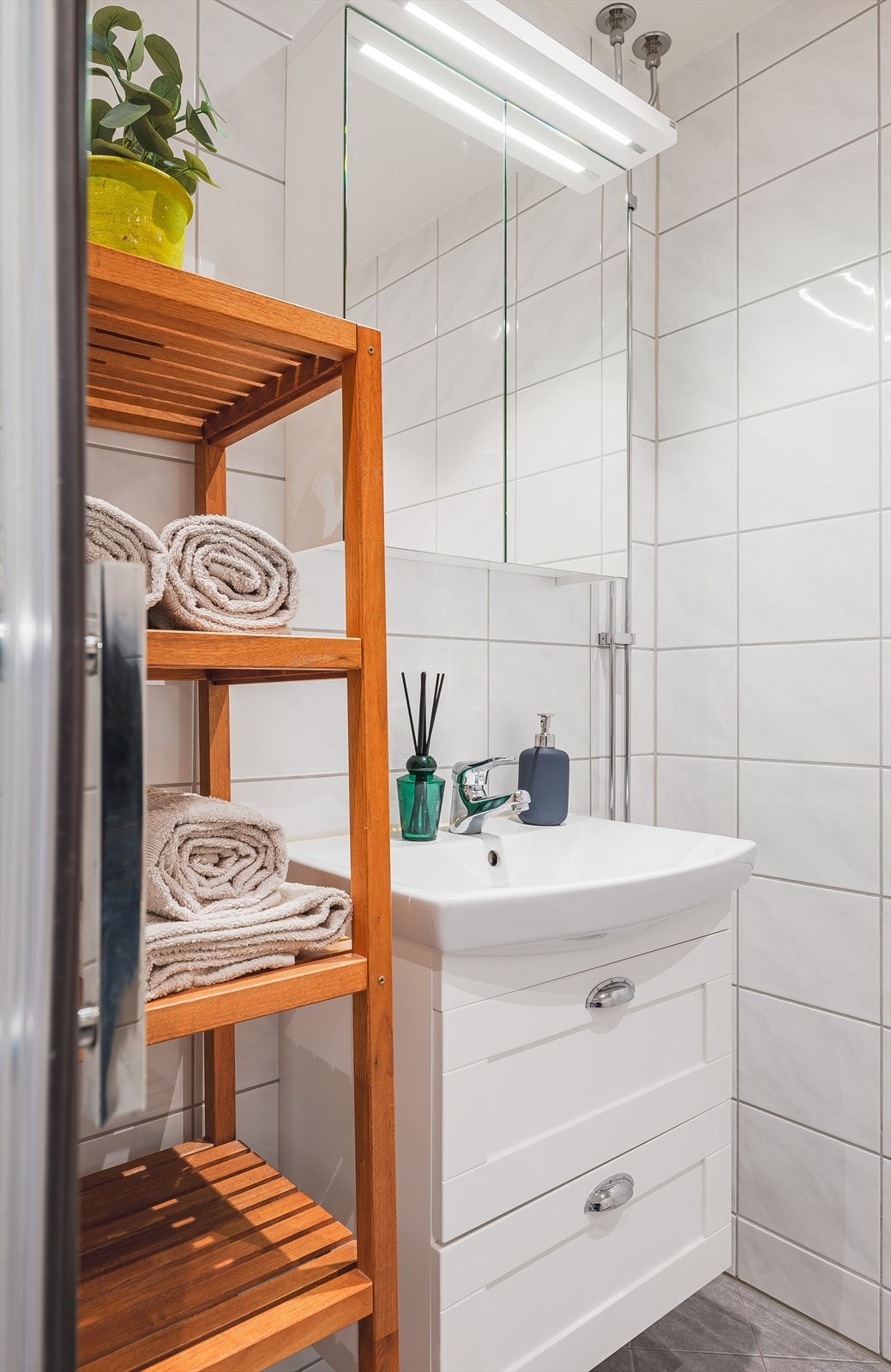 Lys baderomsinnredning med skuffer og ovenpåliggende servant, vegghengt speilskap med belysning over. Baderommet er også utstyrt med dusjhjørne med innfellbare glassdører og opplegg for vaskemaskin. Galleribilde