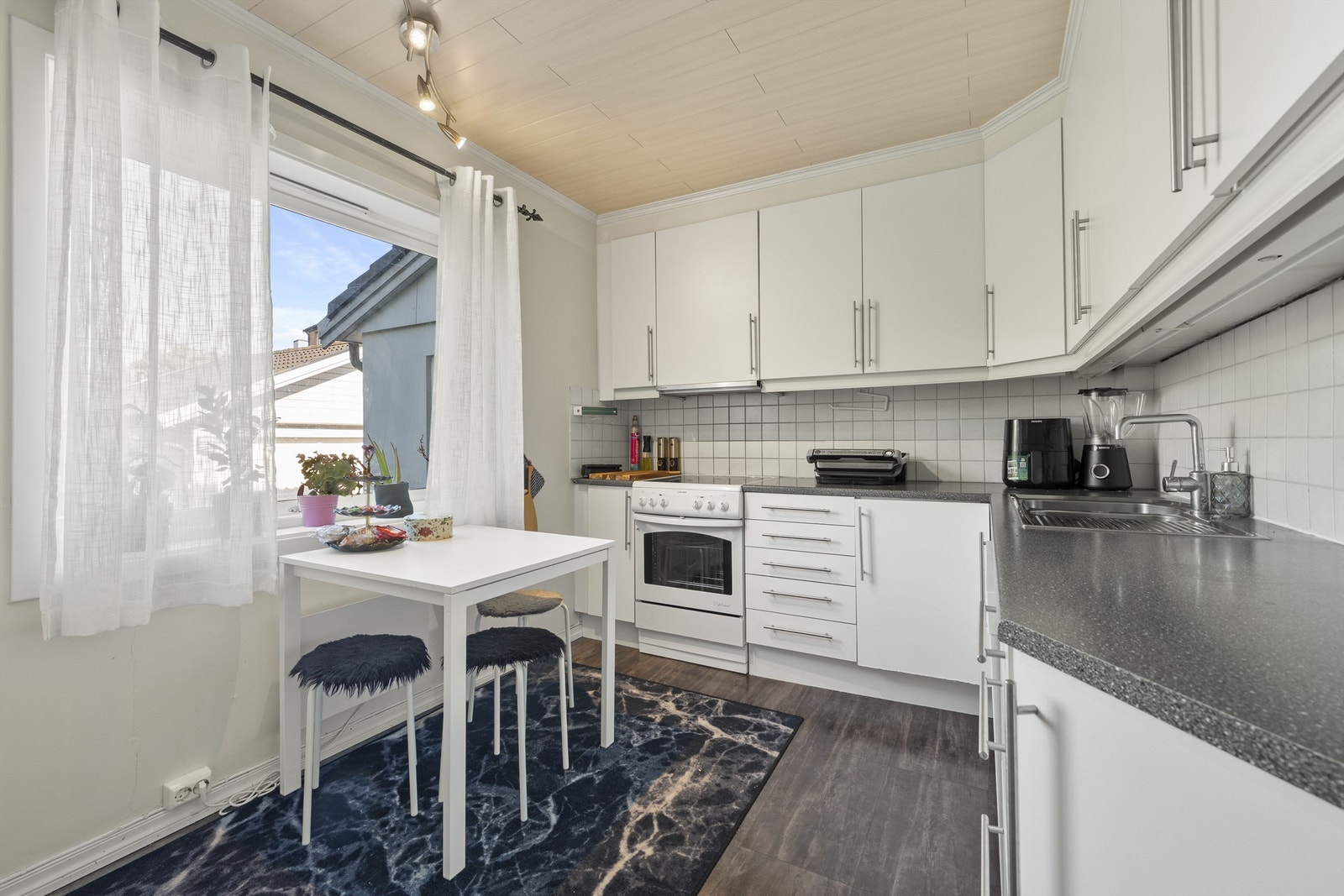 Funksjonelt kjøkken med laminatgulv, kombinerte veggflater i flis og malte slette flater, samt himling med takbord Galleribilde