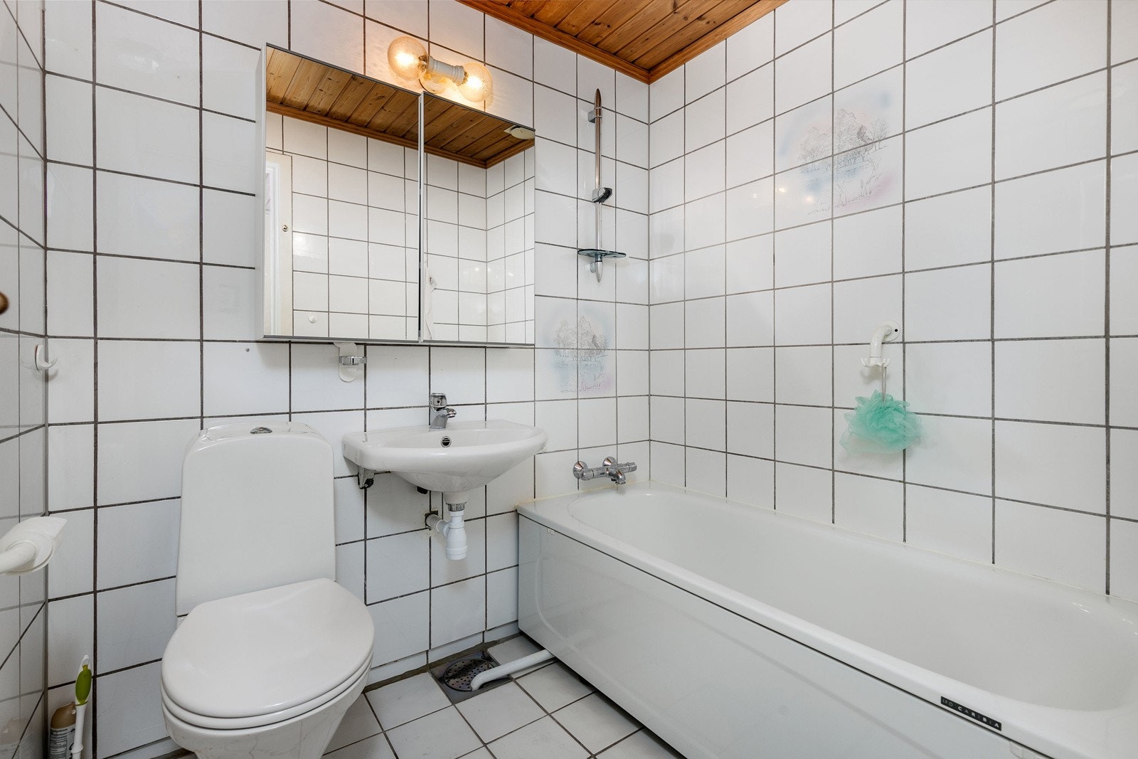 Eldre flislagt bad i 2. etasje med varmekabler i gulv. Baderomsinnredningen består av overskap med speilfronter og servant. Videre har badet dusj i badekar og gulvstående toalett. Galleribilde