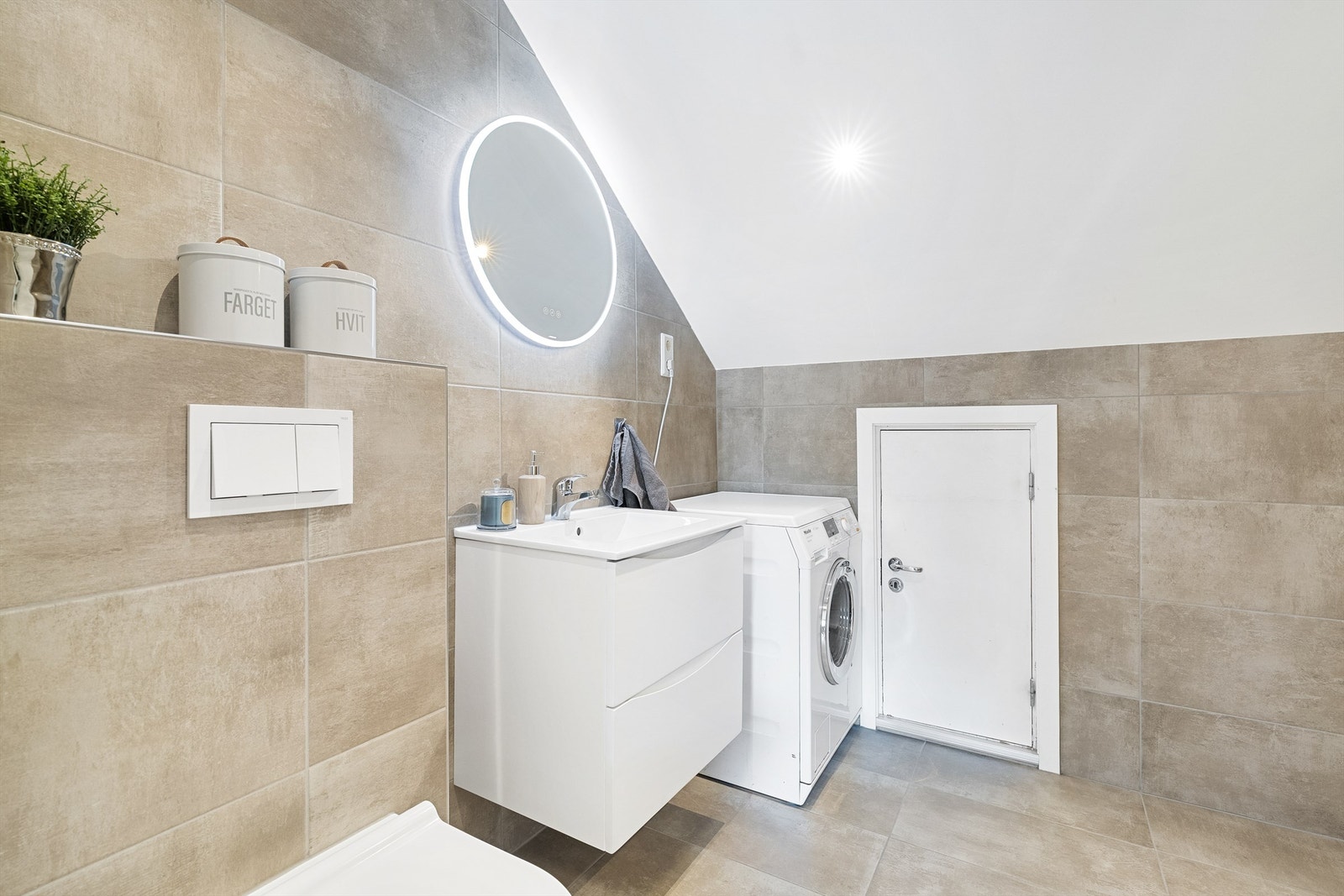 Badet er innredet med veggehengt servantskap med skuffer, speil med lys og stikkontakt på vegg over servant, nedsenket dusjssone og vegghengt toalett Galleribilde