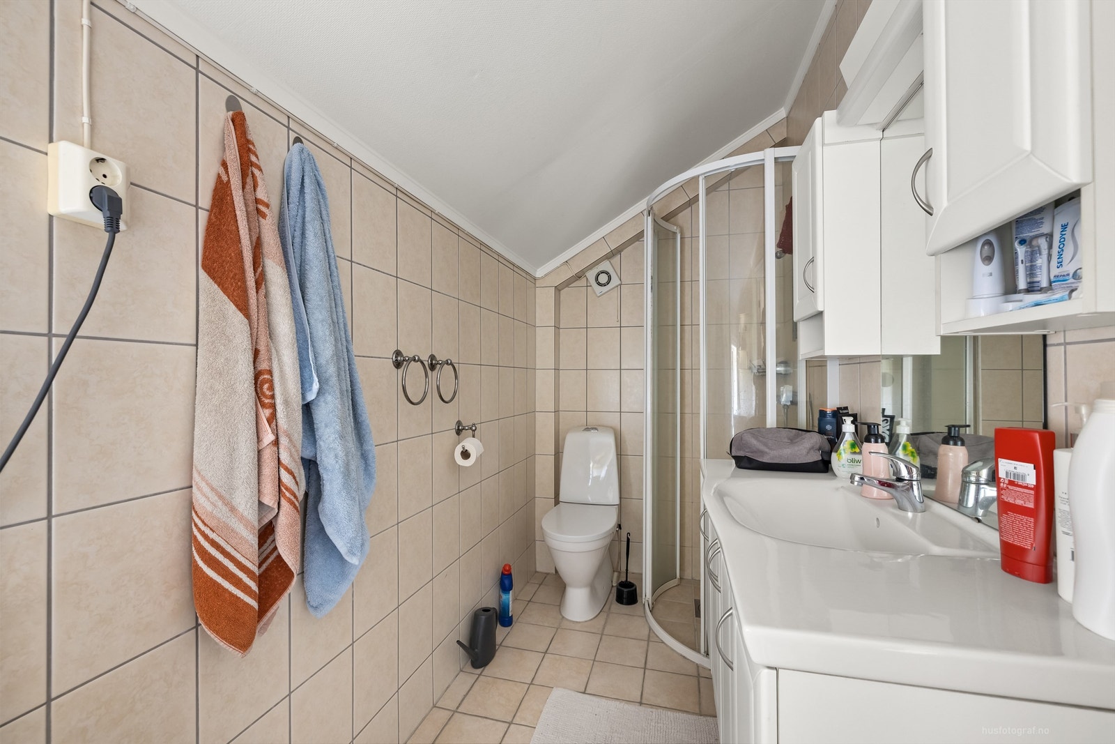 Flislagt bad med varmekabler, gulvstående toalett, dusjhjørne og vegghengt servantinnredning. Galleribilde