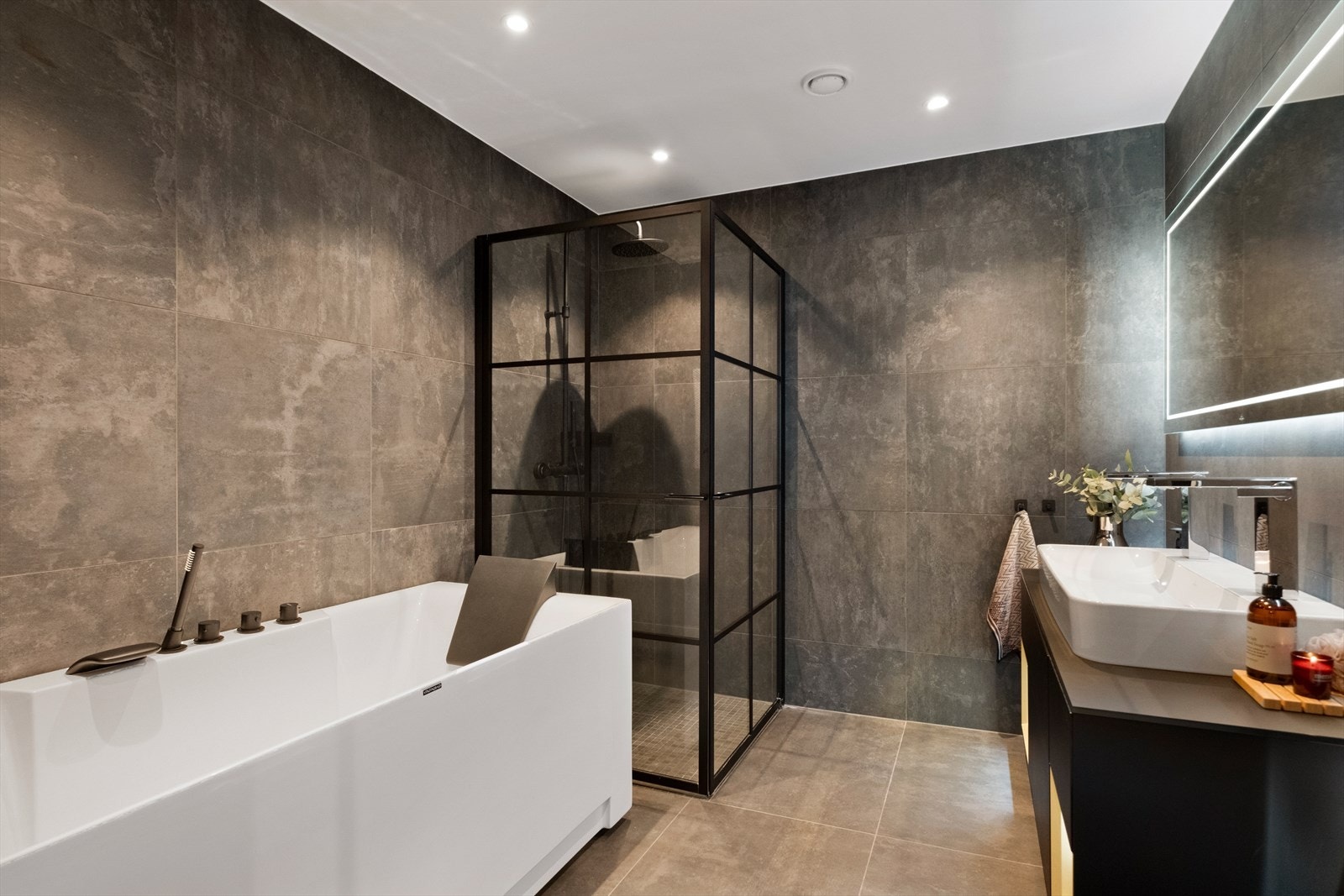 Badet er utstyrt med badekar, spyle/tørketoalett, dusjdører og innredning med servant og to blandebatterier. Galleribilde