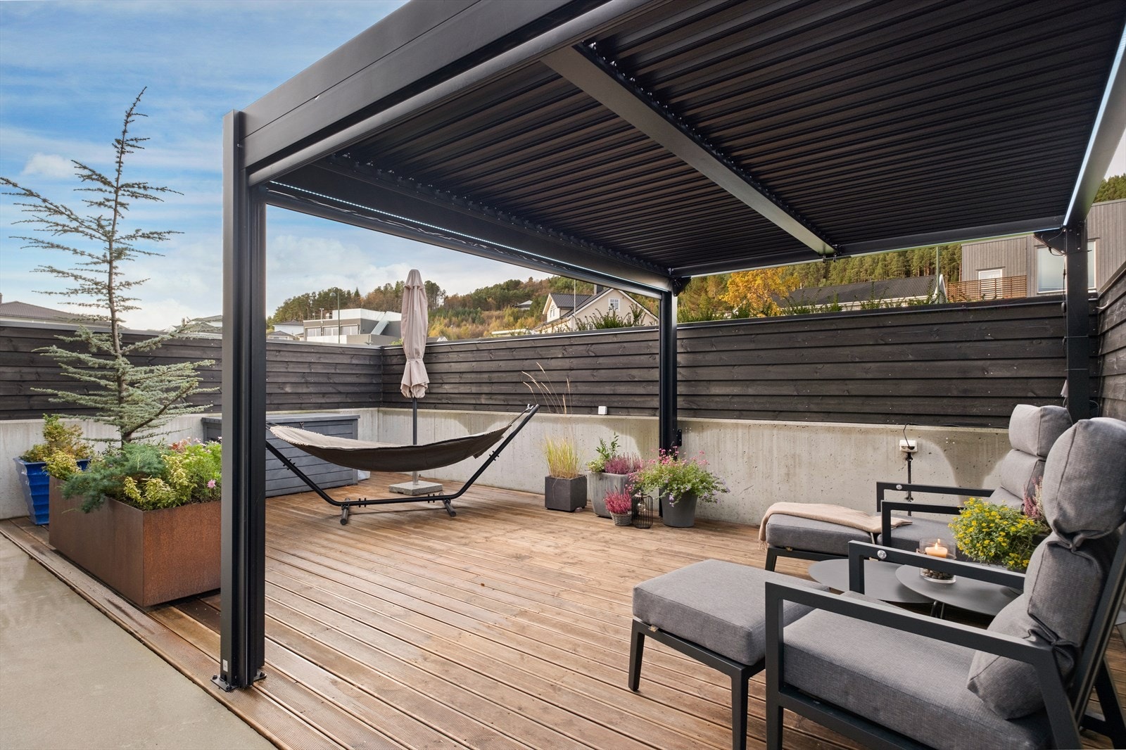 Pergolaen gir skygge til uteplassen, som er belagt med treterrassebord og har en avslappet atmosfære. Galleribilde