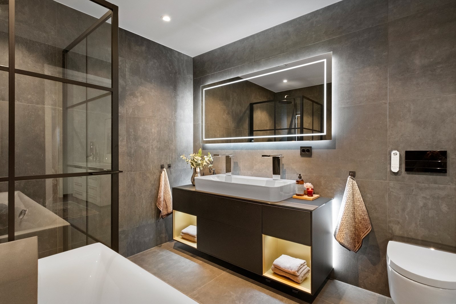 Badet er utstyrt med badekar, spyle/tørketoalett, dusjdører og innredning med servant og to blandebatterier Galleribilde