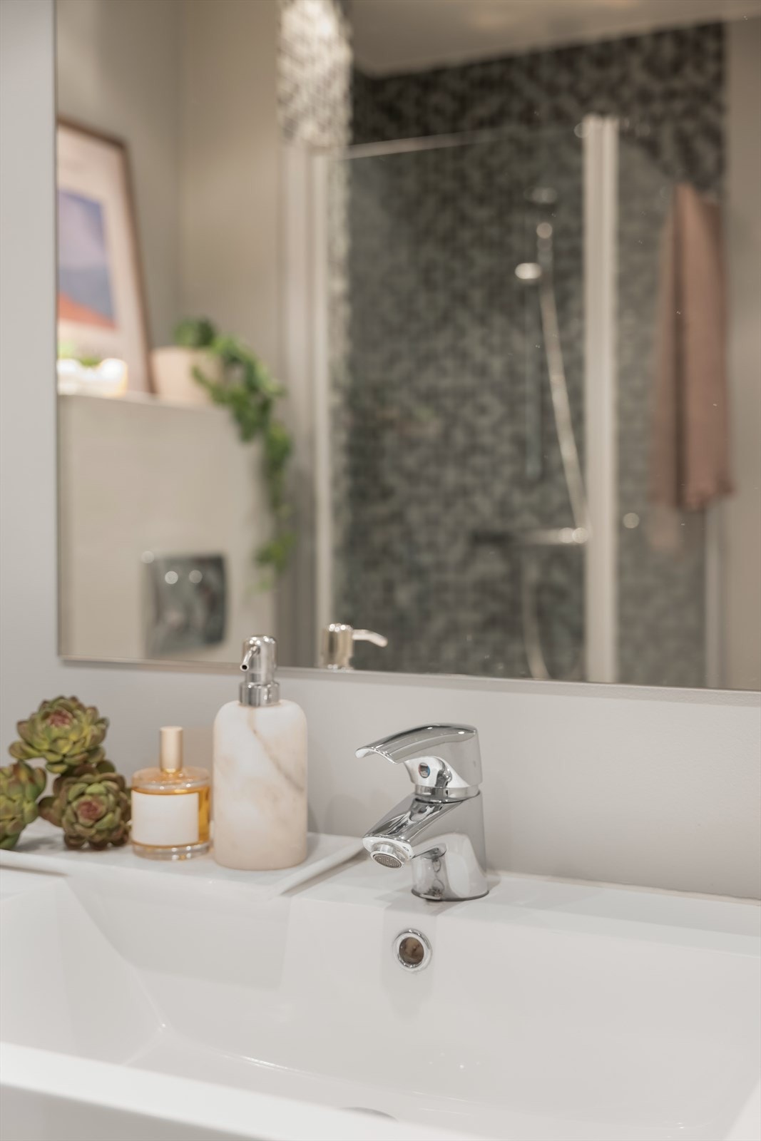 Innredningen inkluderer servant med skuffeseksjon, speil med overlys, vegghengt toalett og et dusjhjørne med svingbare glassdører. Galleribilde