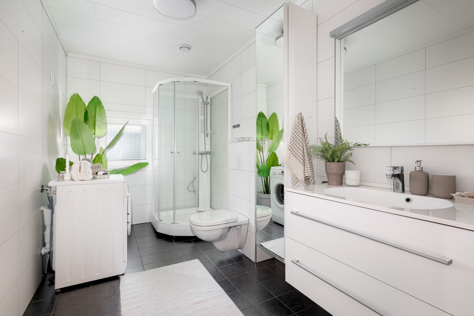 Pent helfliset bad. Badet har innredning med skuffer og heldekkende servant, samt speil på vegg med overlys. Badet er også innredet med dusjkabinett og veggmontert toalett. Det er opplegg for vaskemaskin. Galleribilde