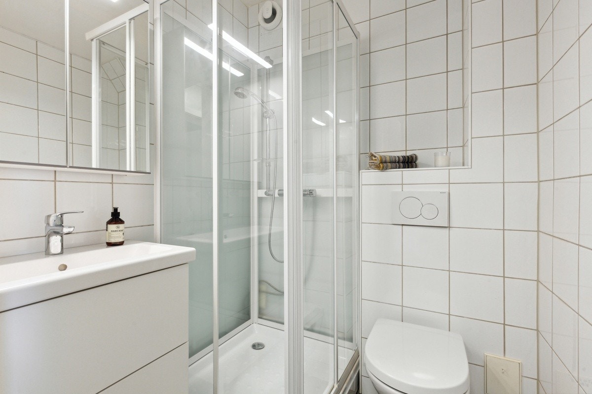 Leilighetens bad inneholder baderomsinnredning, dusjkabinett og WC Galleribilde