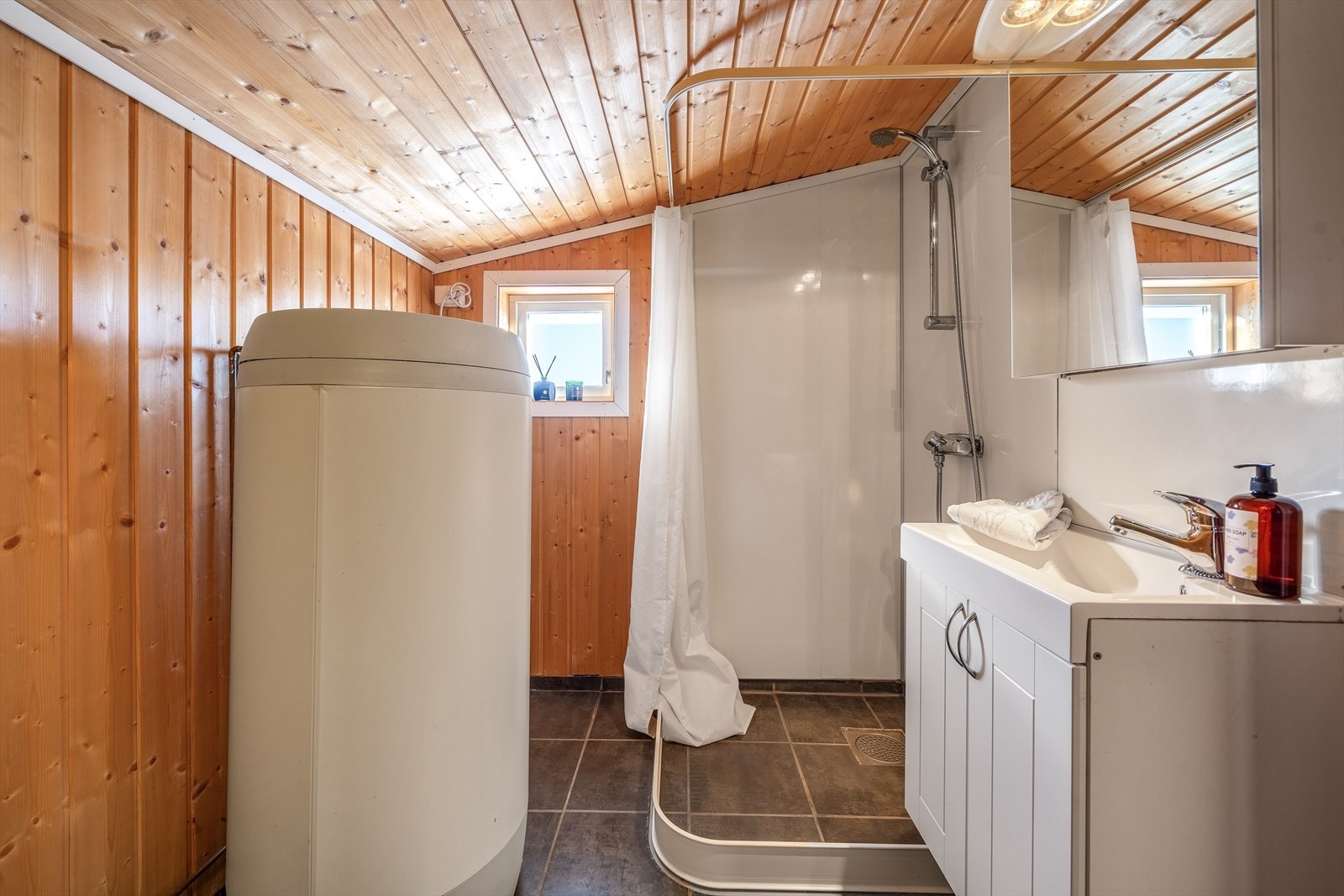 Praktisk og funksjonelt baderom med fliser og varmekabler på gulv. Dusjsonen har bedre romspalte for oppbevaring, og vegger og himling er kledd med furupanel. Galleribilde