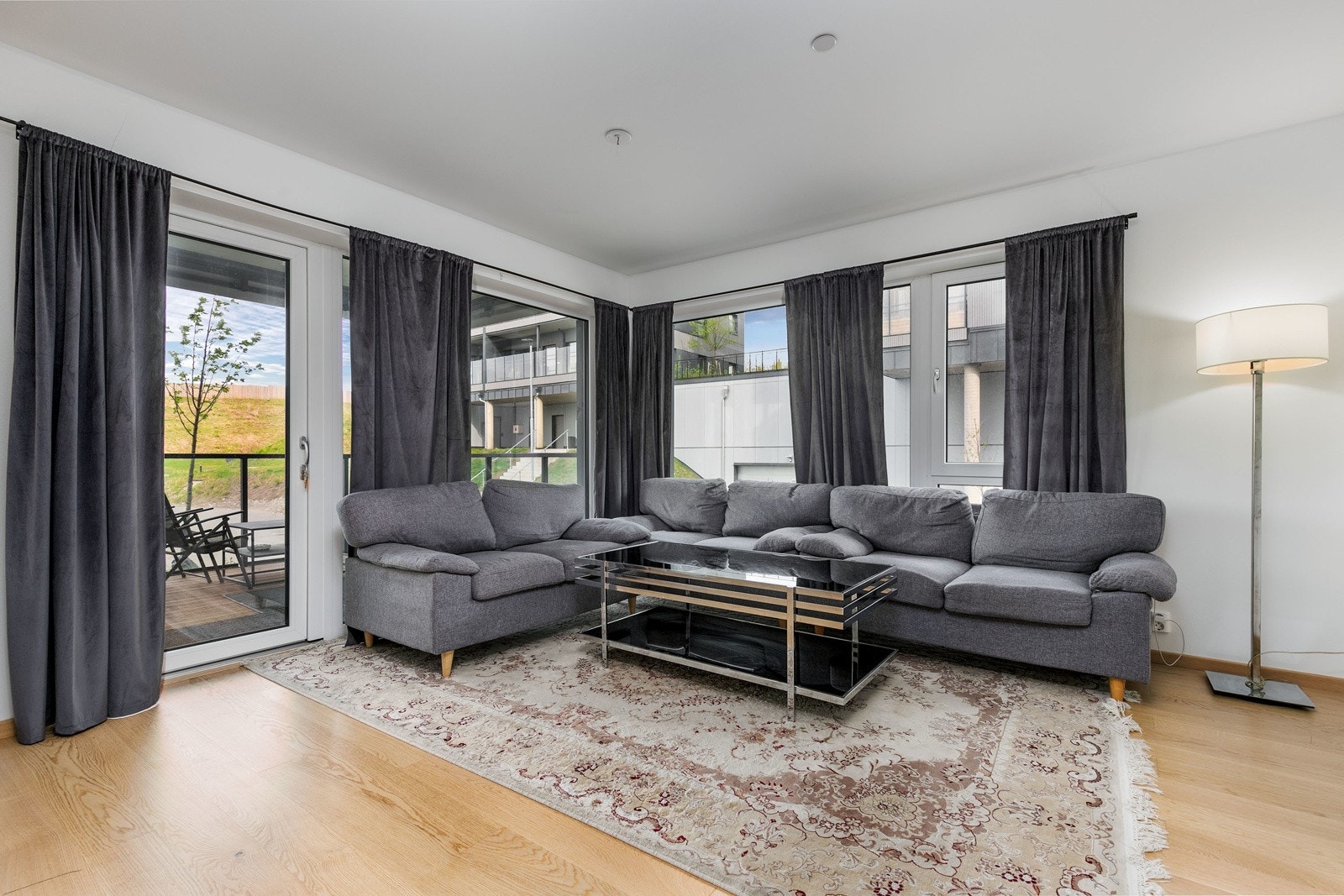 Den åpne stuen fremstår som innbydende i lyse fargevalg. Store vindusflater fra gulv til tak slipper inn rikelig med lys og den flotte takhøyden på hele 2,49 meter gir en luftig romfølelse Galleribilde