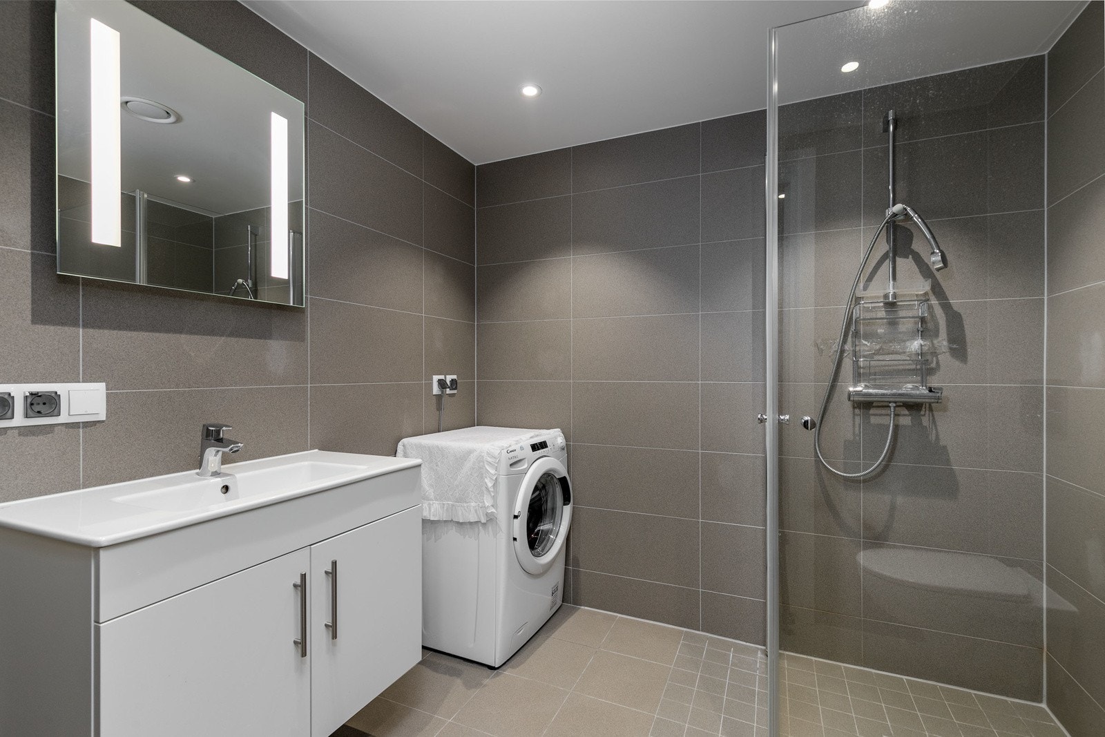 Smakfullt bad fra 2022 med flislagte overflater og varmekabler i gulv. Innredningen består av moderne skapinnredning med heldekkende hvit vask og vegghengt speil med integrert LED lys. Galleribilde