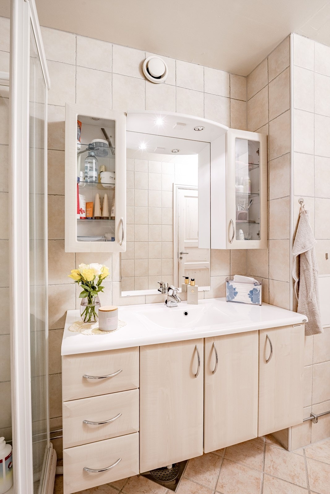 Pen baderomsinnredning med lyse fronter og heldekkende servant, speil med belysning og vegghengte skap over. Baderommet er også utstyrt med dusjkabinett og gulvstående toalett. Galleribilde