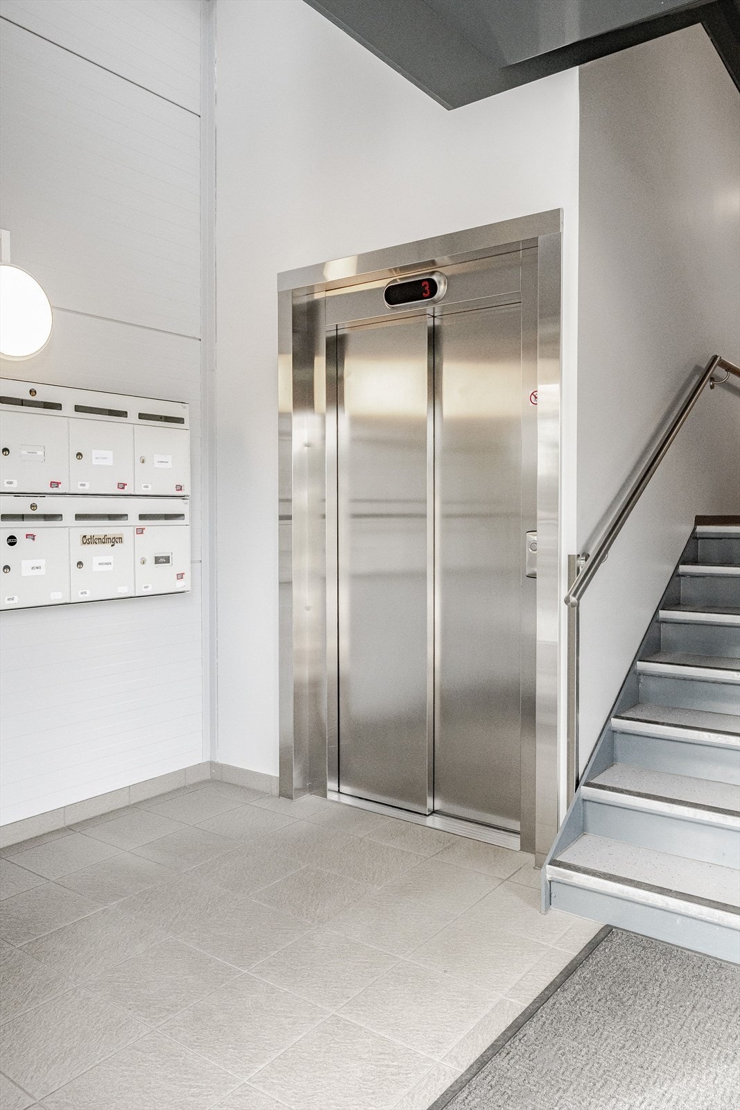 Flislagt inngangsparti med postkasser og heis. Galleribilde