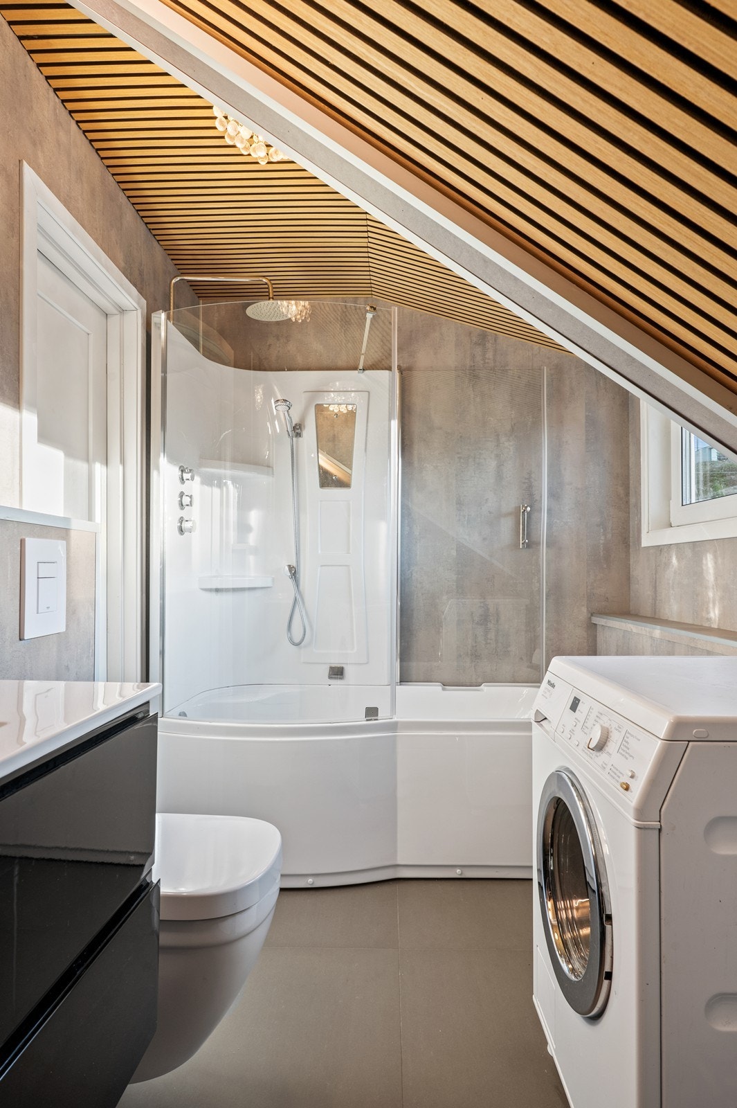 Delikat bad fra 2024 i 2. etasje med baderomsplater på vegg samt fliser på gulv. Innredning med bl.a. badekar og opplegg for vaskemaskin Galleribilde