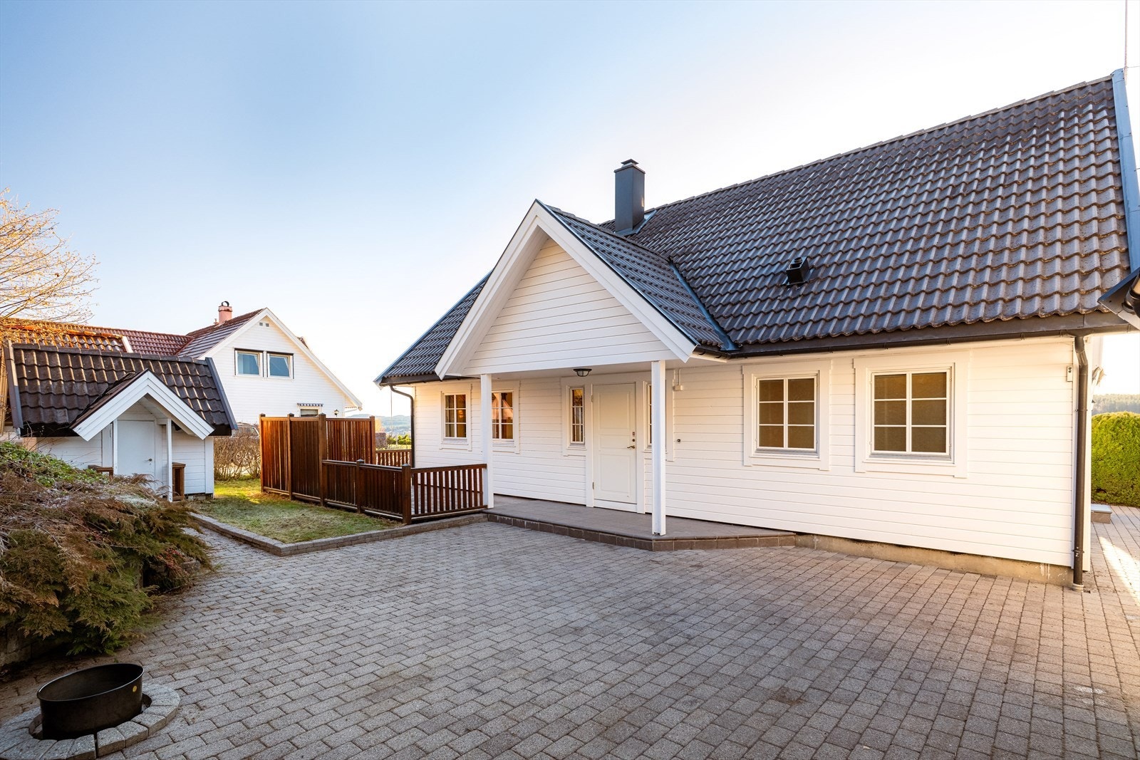 Romslig og ryddig gårdsplass med belegningsstein og kantstein. Det er gruset innkjørsel og parkering i dobbelgarasje. Galleribilde