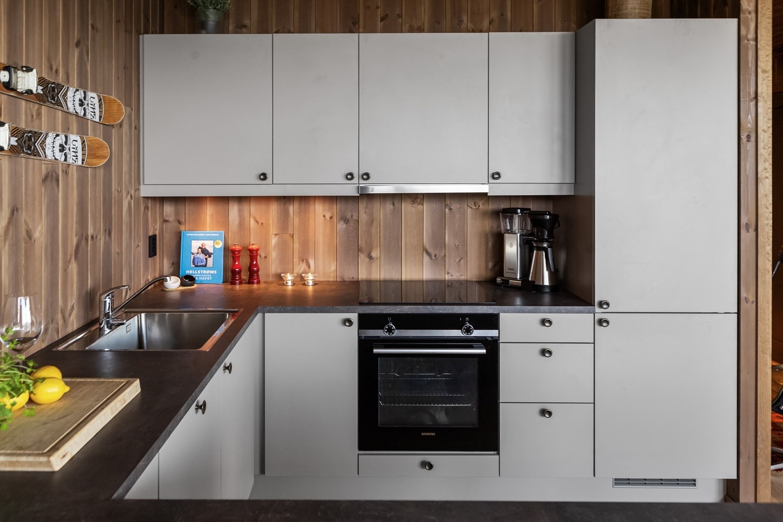 Innredningen har overskap på én side, hvite, slette fronter og grå benkeplate i laminat med stor, planlimt oppvaskkum. Alle hvitevarer er integrert og består av koketopp, stekeovn, oppvaskmaskin og kjøl/frys. Galleribilde