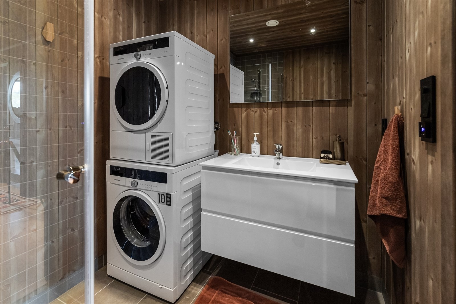 Hovedbadet har et stilrent baderomsmøblement og opplegg for vaskemaskin i søyleløsning. Baderomsmøblementet består av veggengt skuffeseksjon med hvite høyglansfronter, heldekkende servant og speil. Galleribilde