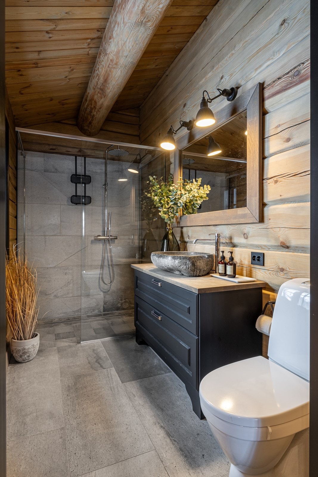 Hovedbadet har et stilrent uttrykk, der store, grå gulvfliser kombineres med tømmer og matchende fliser på veggene. Galleribilde