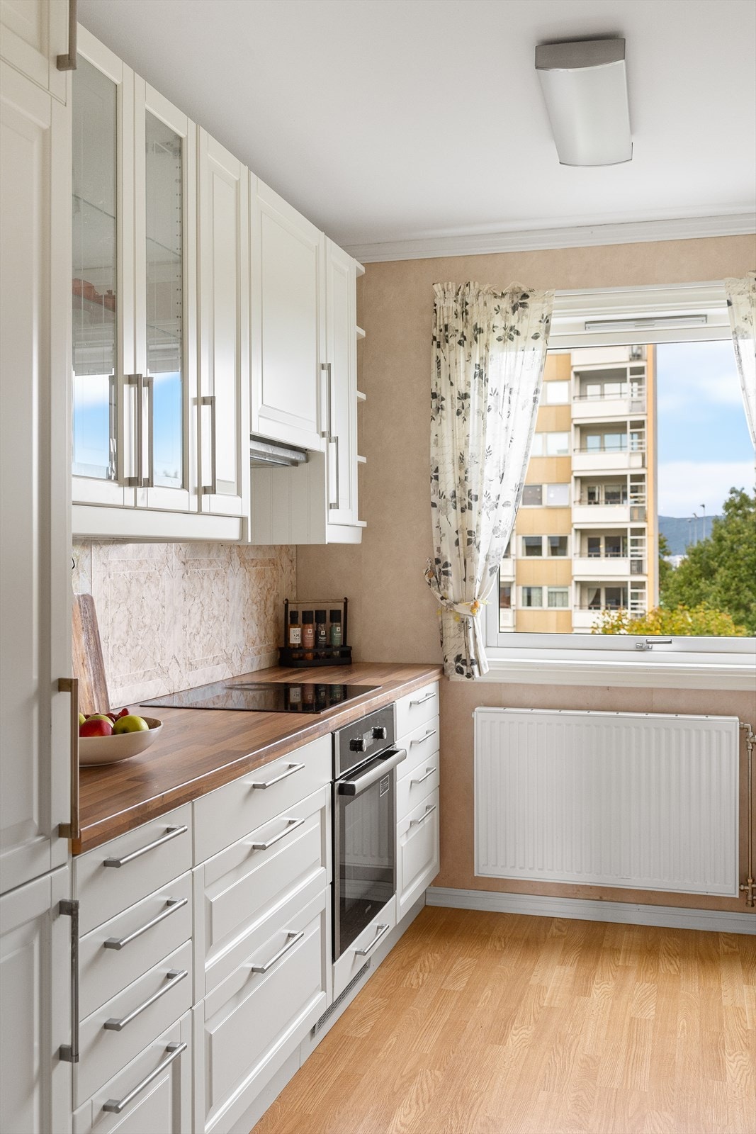 Stilrent kjøkken bestående av hvite, profilerte fronter og benkeplate av laminat med nedfelt kum i rustfritt stål og belysning under overskap. Galleribilde