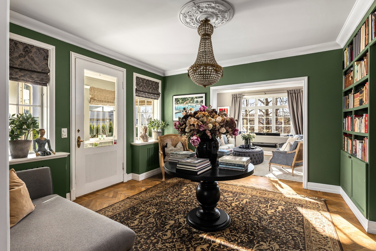 Stuen mellom hovedstue og spisestue er innredet med plassbygde bokhyller og har en vakker takrosett og utgang til vintehagen.
