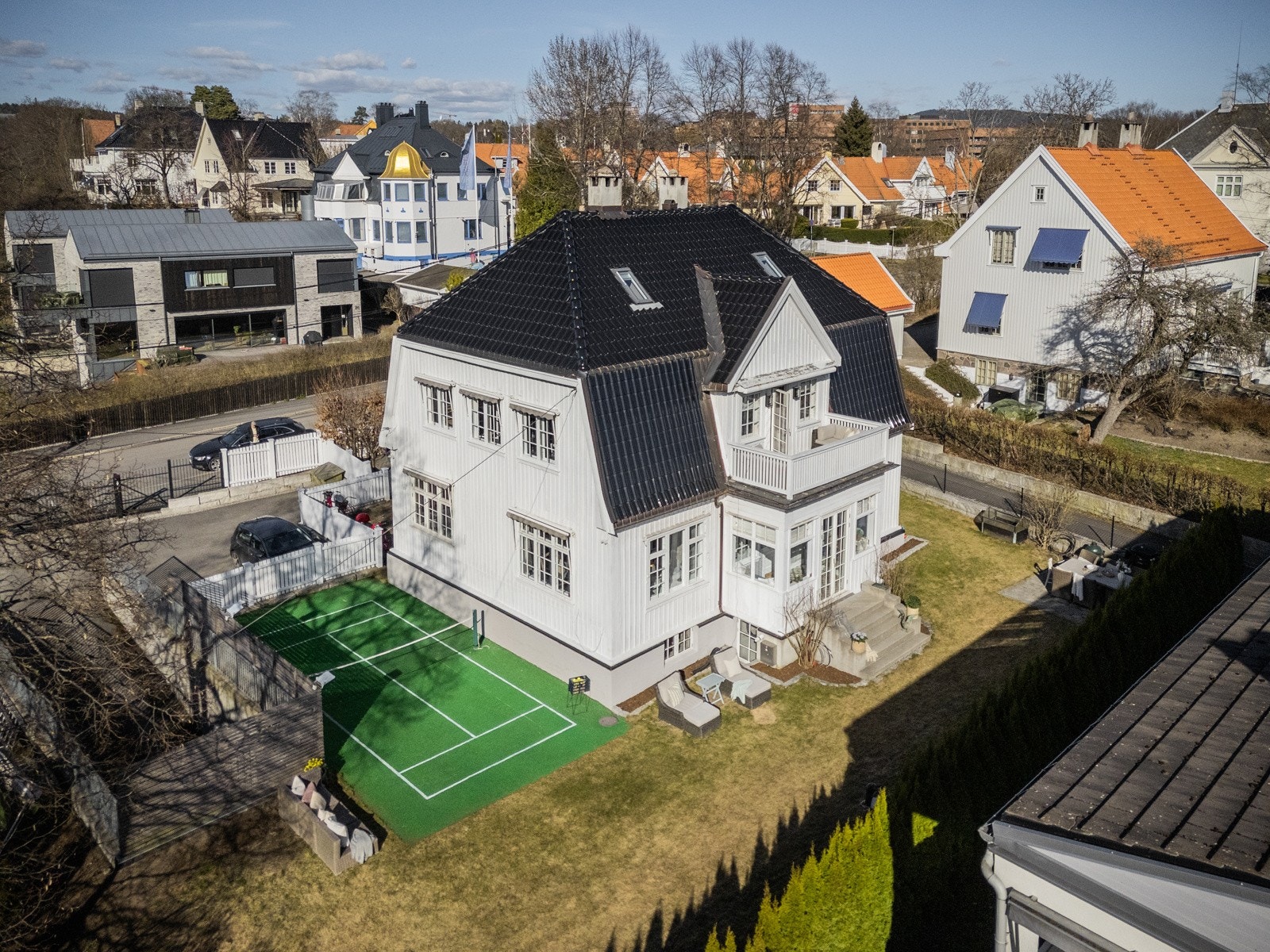 Villaen strekker seg over fire plan, med hvitmalt kledning og mansardtak med sort, glassert takstein.