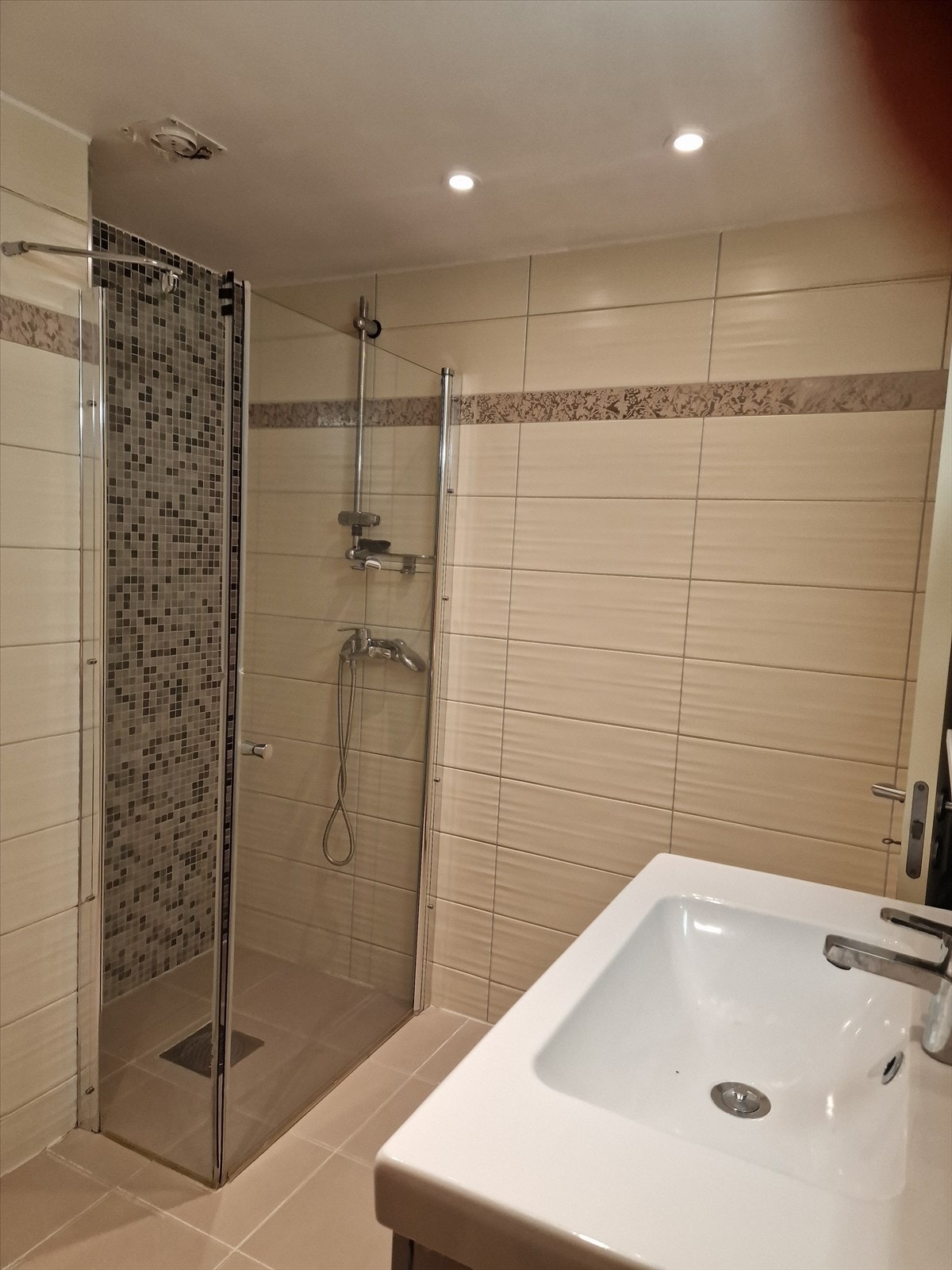 Flislagt bad med toalett, servant, oppbevaringsmuligheter og dusj med glassvegger. Galleribilde