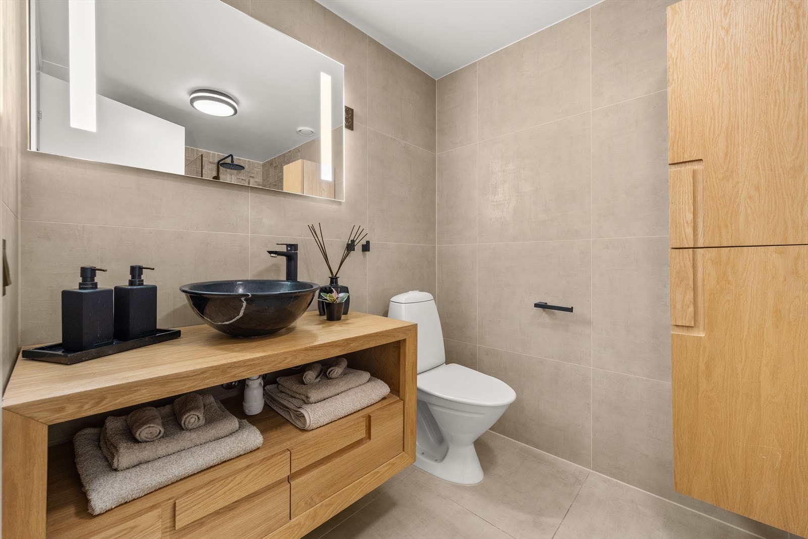 Pent bad som er oppgradert med flis på flis i 2018, samt ny innredning bestående av vegghengt skap med servantbolle, speil med lys, veggskap, toalett og dusjnisje med glassfører og regndusj Galleribilde