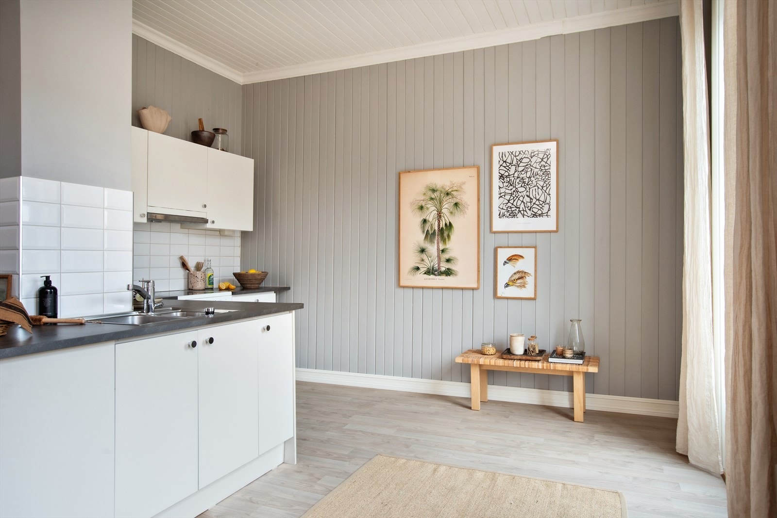 Enkel kjøkkeninnredning med slette fronter, fliser og belysning over laminat benkeplate m/ nedfelt oppvaskkum og blandebatteri. Galleribilde