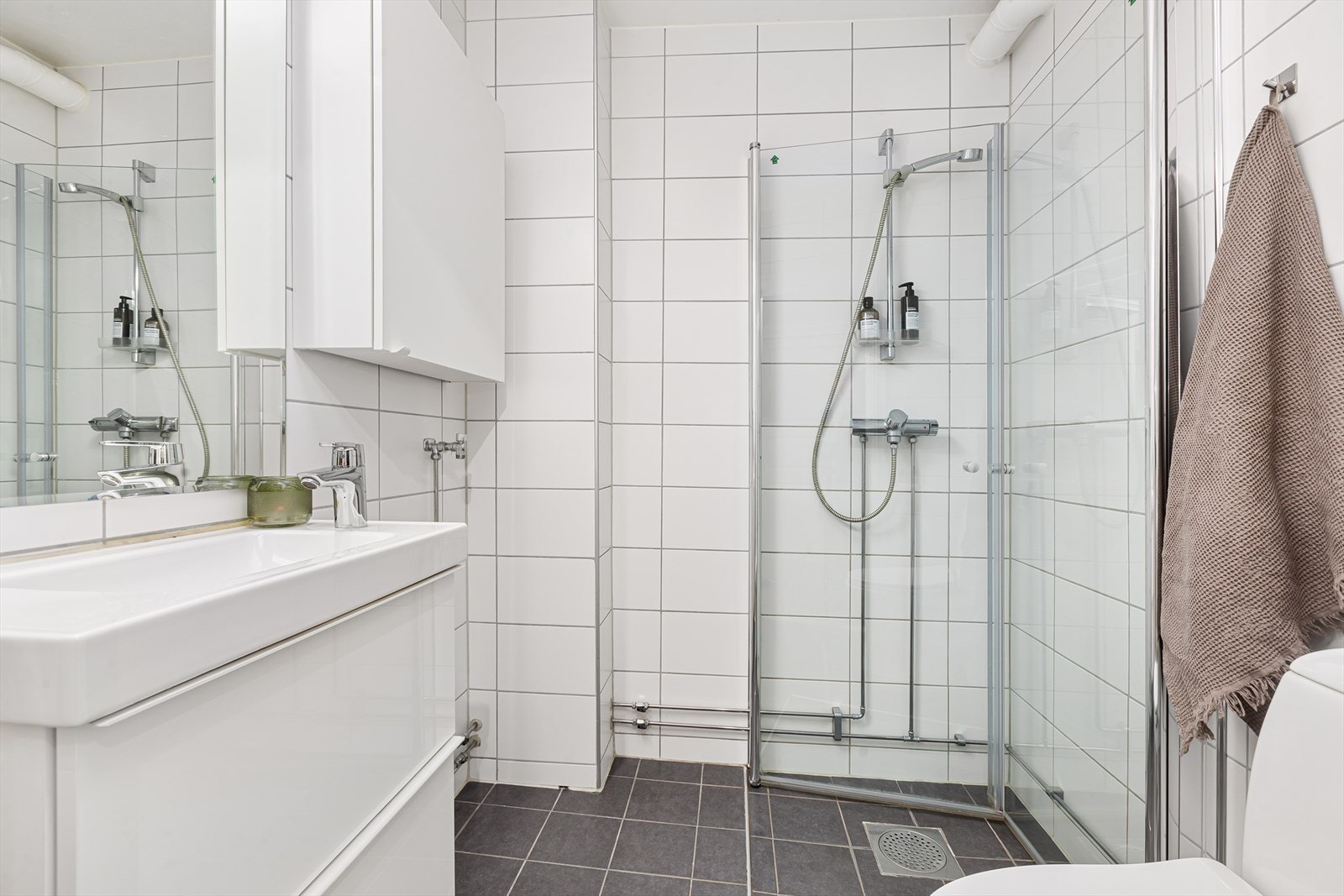 Pent flislagt bad fra 2017/2018 med innredning bestående av klosett, dusjhjørne med innfellbare dører, veggskap og baderomsinnredning med speil og lysarmatur Galleribilde