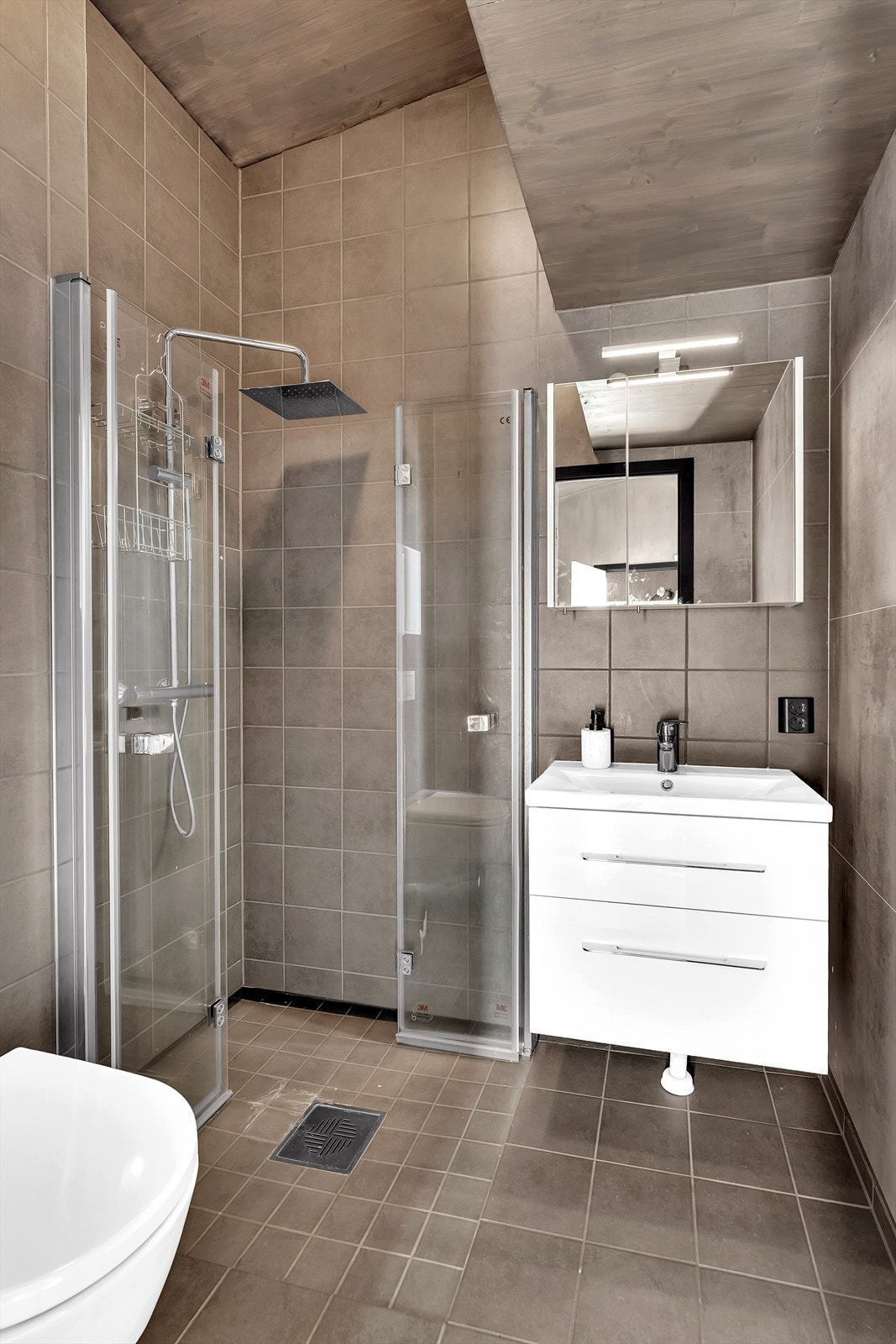 Badet er utstyrt med nedfelt servant, speilskap med belysning, veggmontert toalett og dusjnisje. Galleribilde