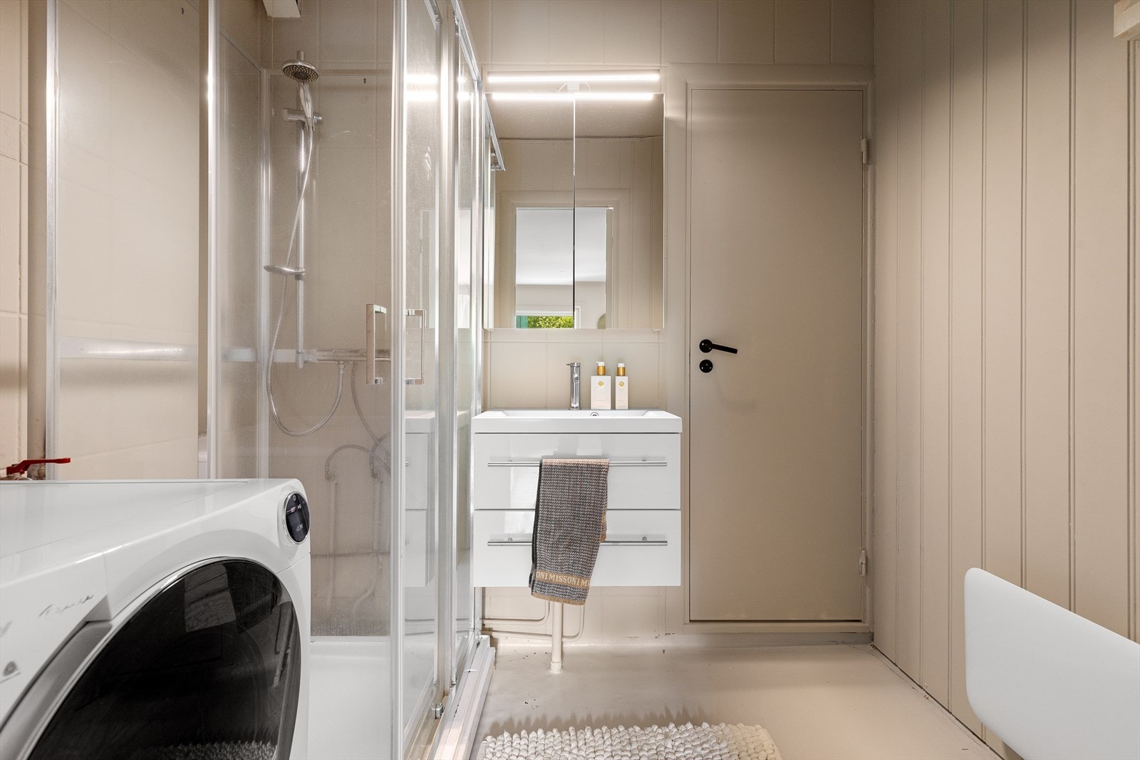 Eldre bad med dusjkabinett, moderne vegghengt innredning og opplegg for vaskemaskin Galleribilde