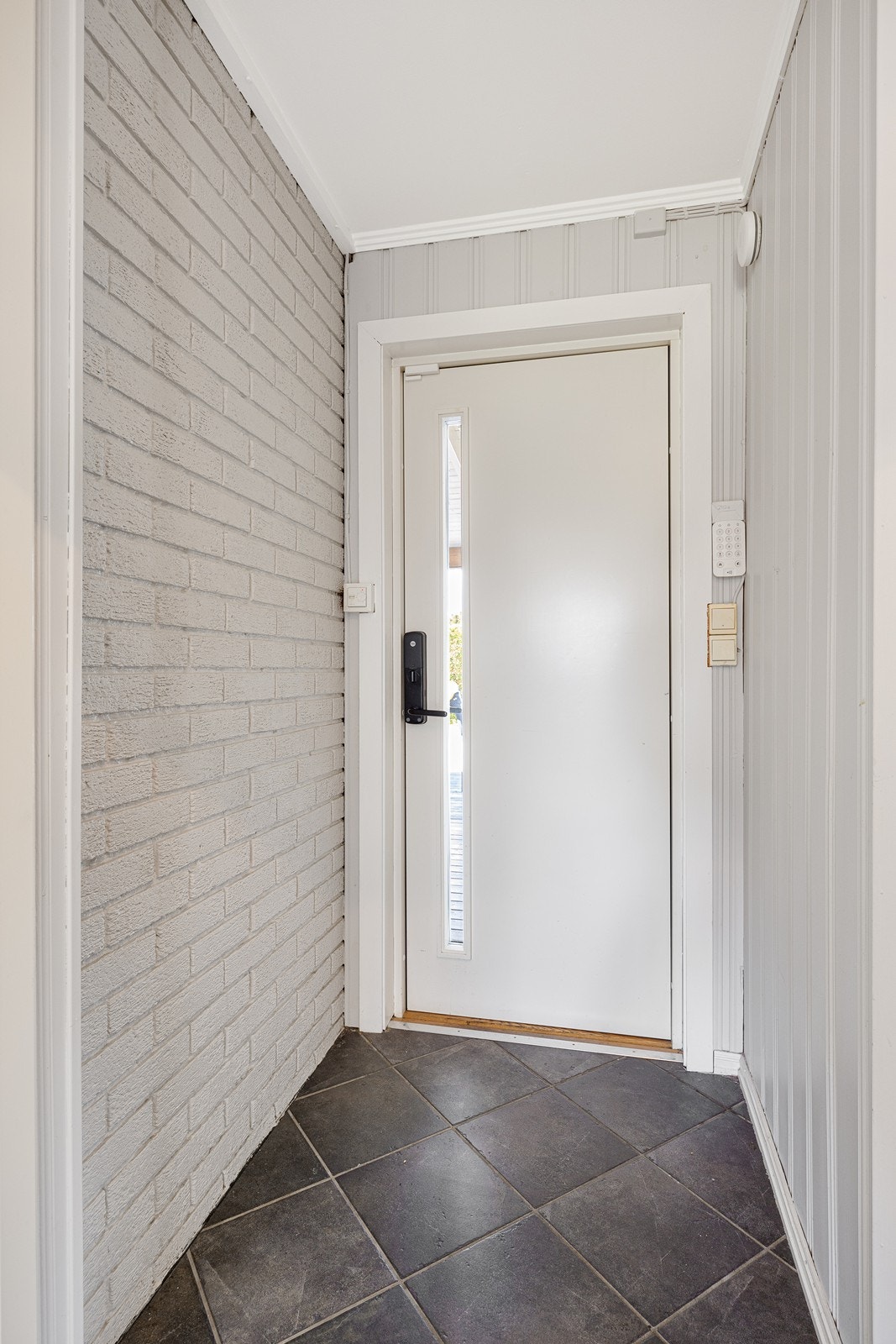 Vel inne blir vi ønsket velkommen i en fin entré med lysmalt panel på veggene og grå fliser på gulvet. Entrédøren er utstyrt med elektronisk dørlås. Galleribilde
