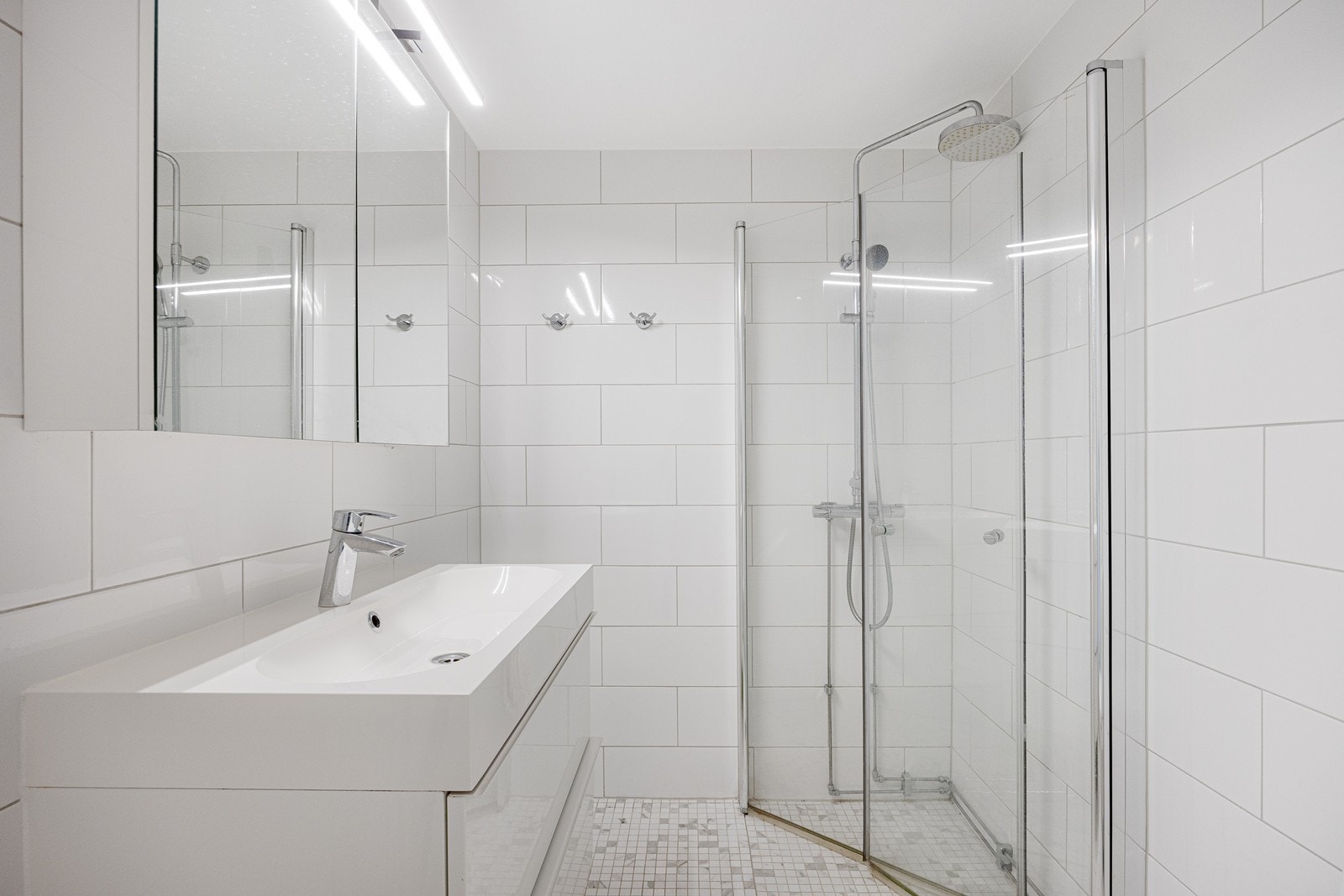 Badet ligger ved soverommene i underetasjen, og fremstår som velholdt og pent. Her er det hvite fliser på veggene og lyse mosaikkfliser på gulv med gulvvarme. Galleribilde