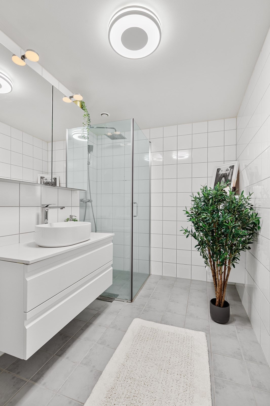 Badet er romslig og utstyrt med baderomsinnredning, servantbolle, speilskap med lys, toalett og dusjnisje med glassdører og regndusj Galleribilde