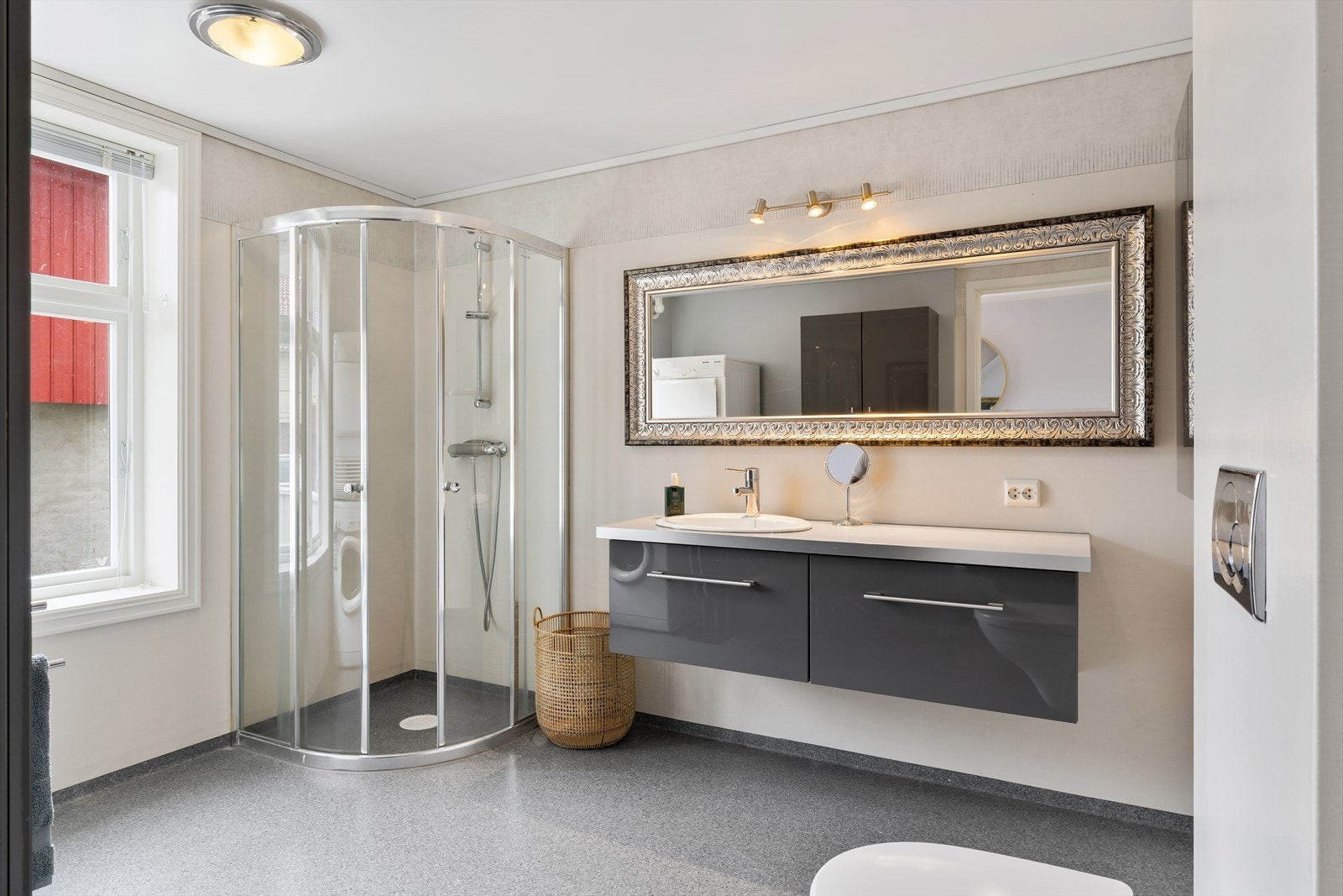 Badet har vinylbelegg på gulv og vegger. Innredning med nedfelt servant, veggmontert toalett, dusjhjørne og opplegg for vaskemaskin. Galleribilde