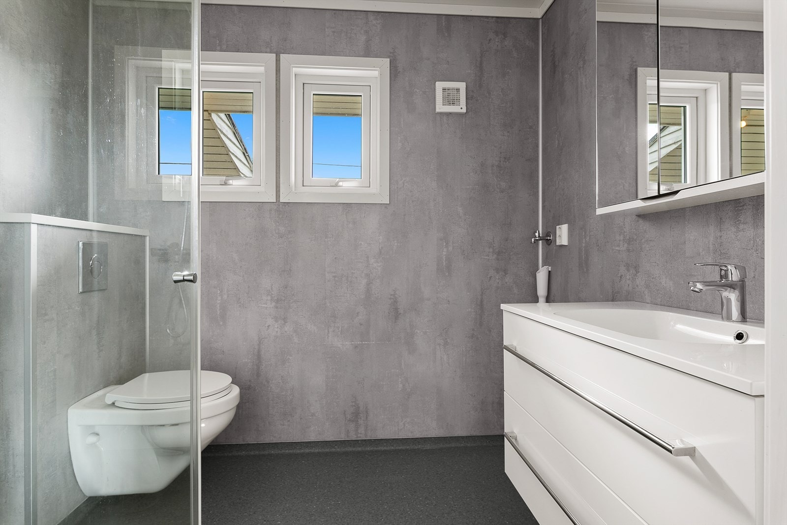 Flott bad bestående av servant m/skap, vegghengt toalett, dusjhjørne og opplegg til vaskemaskin. Galleribilde