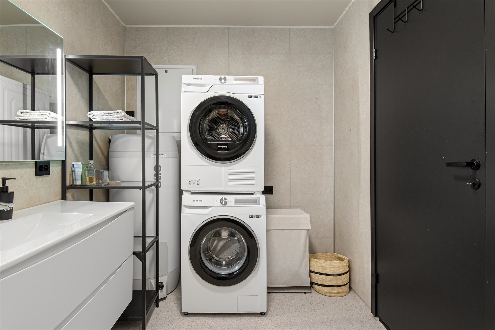 Bad/vaskerom er innredet med dusj, vegghengt toalett, opplegg for vaskemaskin, varmtvannsbereder og servant i innredning med skuffer. Galleribilde