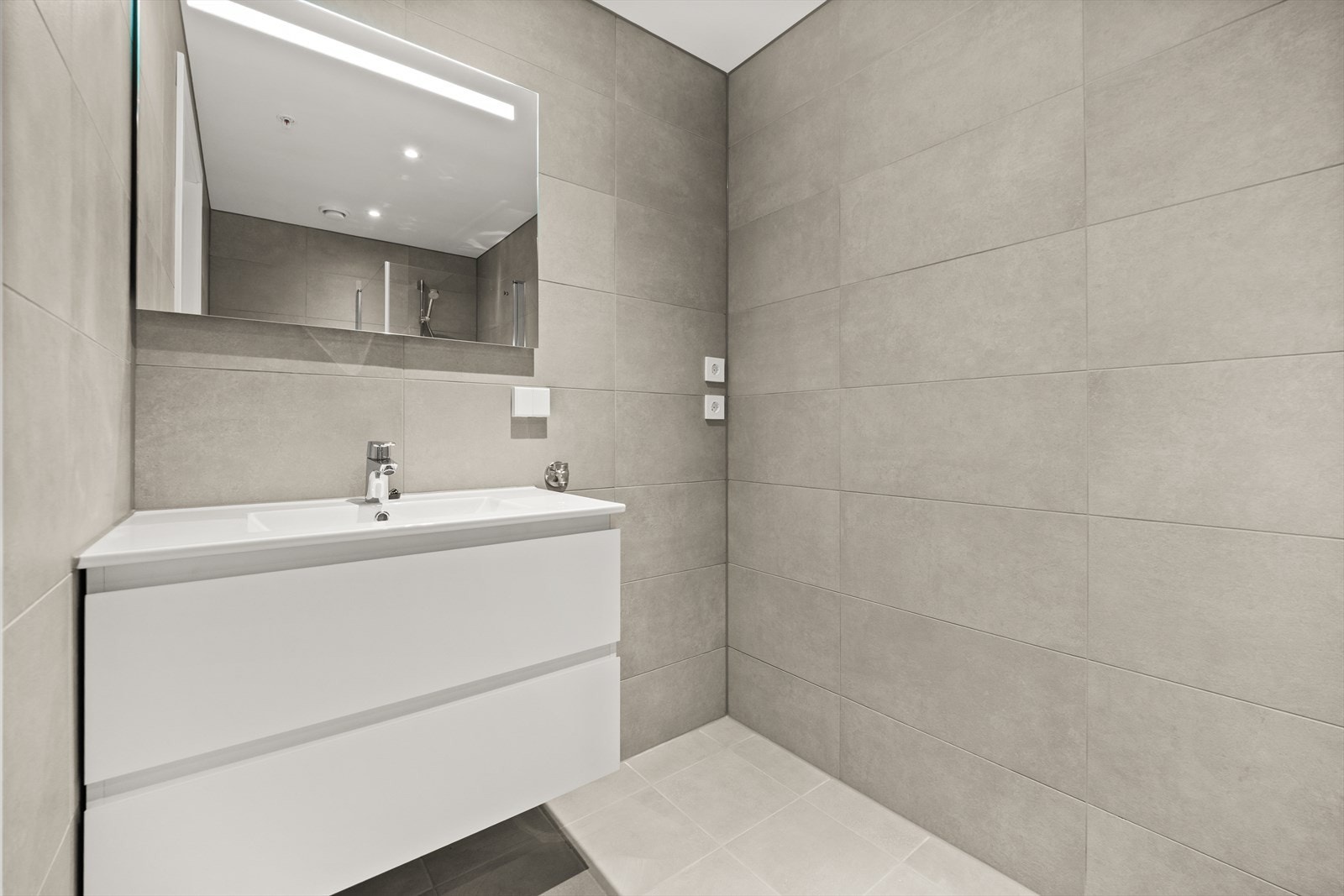 Leiligheten har et fint flislagt bad med vegghengt innredning med tilhørende speil, opplegg for vaskemaskin, dusjhjørne og vegghengt innredning Galleribilde