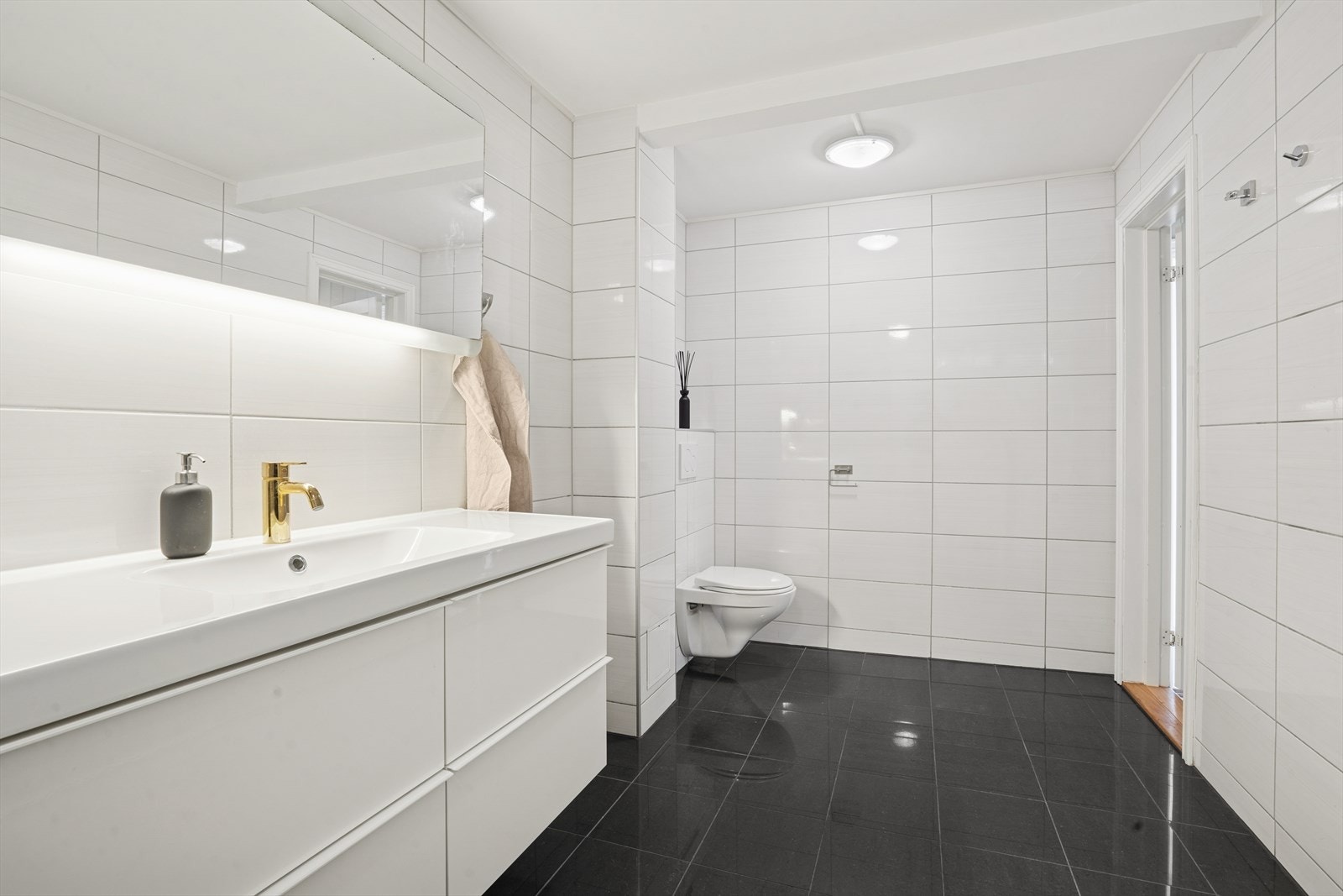 Badet er innredet med servant med skuffer for god oppbevaring, speil med belysning, vegghengt toalett med skjult sisterne og dusj med svingbare glassdører i metallramme. Galleribilde