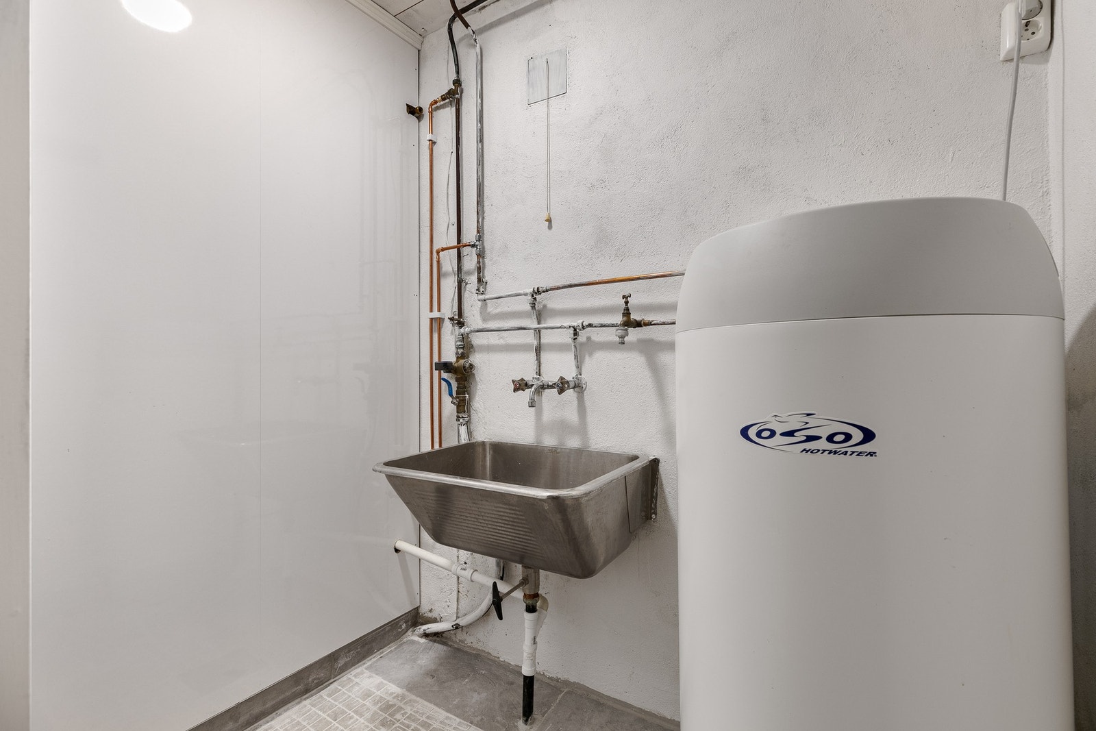 Varmtvannsbereder er plassert i et eget avlukke sammen med en vegghengt utslagsvask - en funksjonell løsning som holder alt samlet og ryddig. Galleribilde