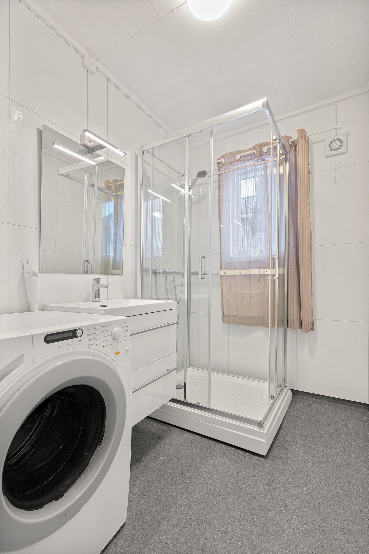 Her finnes vegghengt servantinnredning med ovenpåliggende servant, speilskap med belysning og et praktisk dusjkabinett. Galleribilde