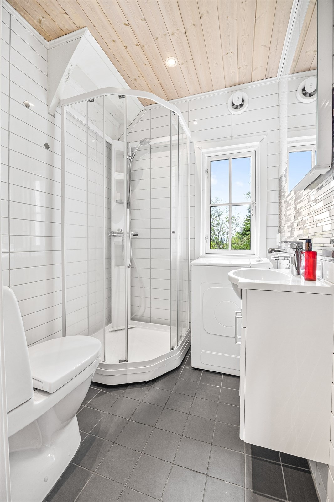 Pent flislagt bad med innredning bestående av klosett, dusjkabinett og servantinnredning med speil Galleribilde