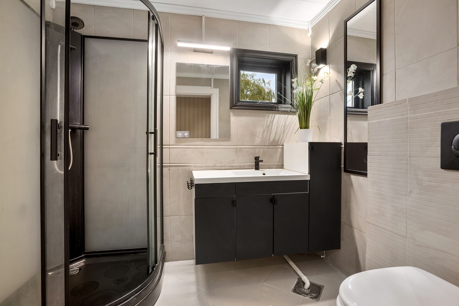 Badet har fliser på gulv og vegger og innredning med sorte fronter - Gjennomført løsning med sort dusjkabinett Galleribilde