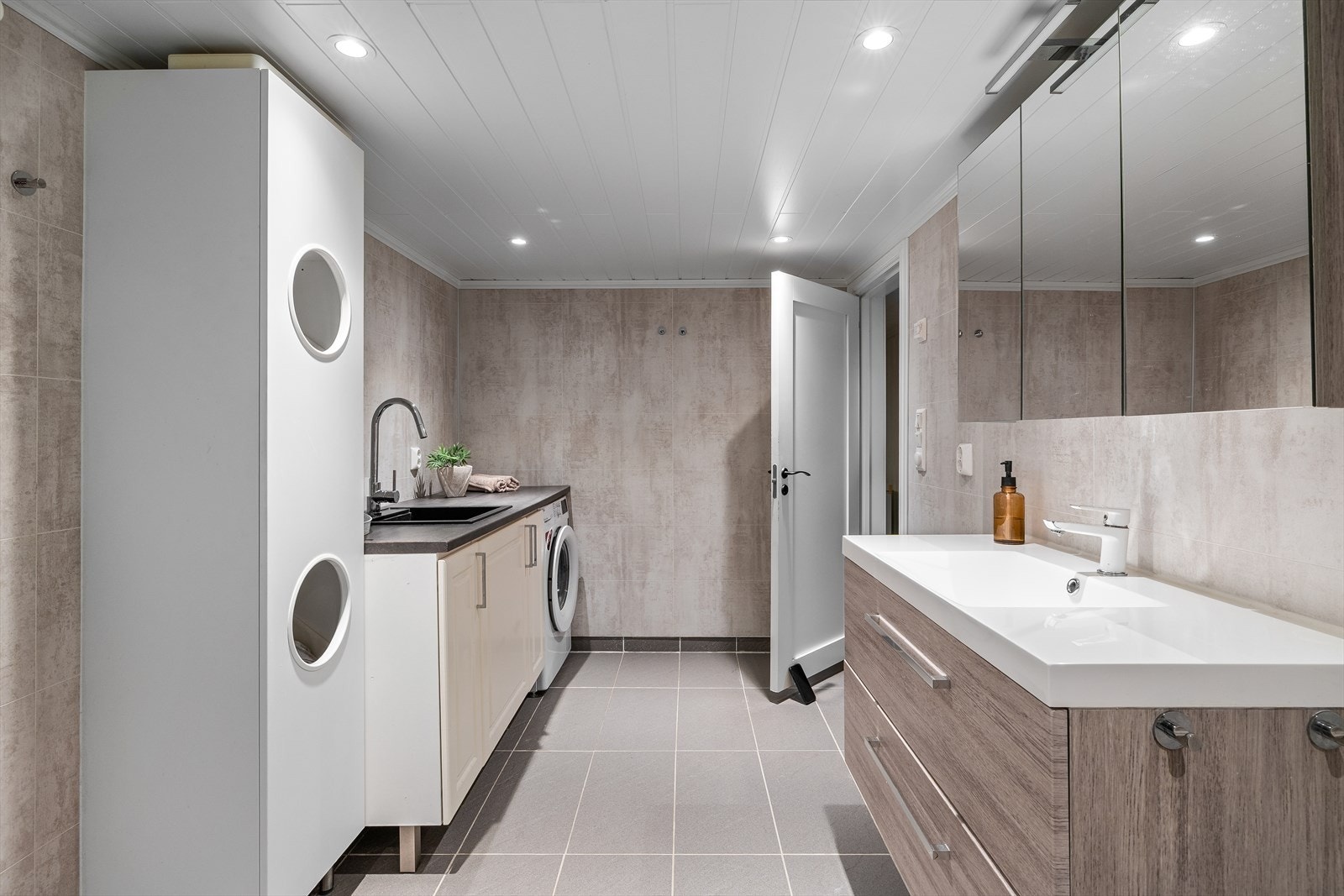 Badet er innredet med veggmontert toalett, badekar, innredning med nedfelt servant og opplegg for vaskemaskin. Det er elektrisk styrt vifte Galleribilde