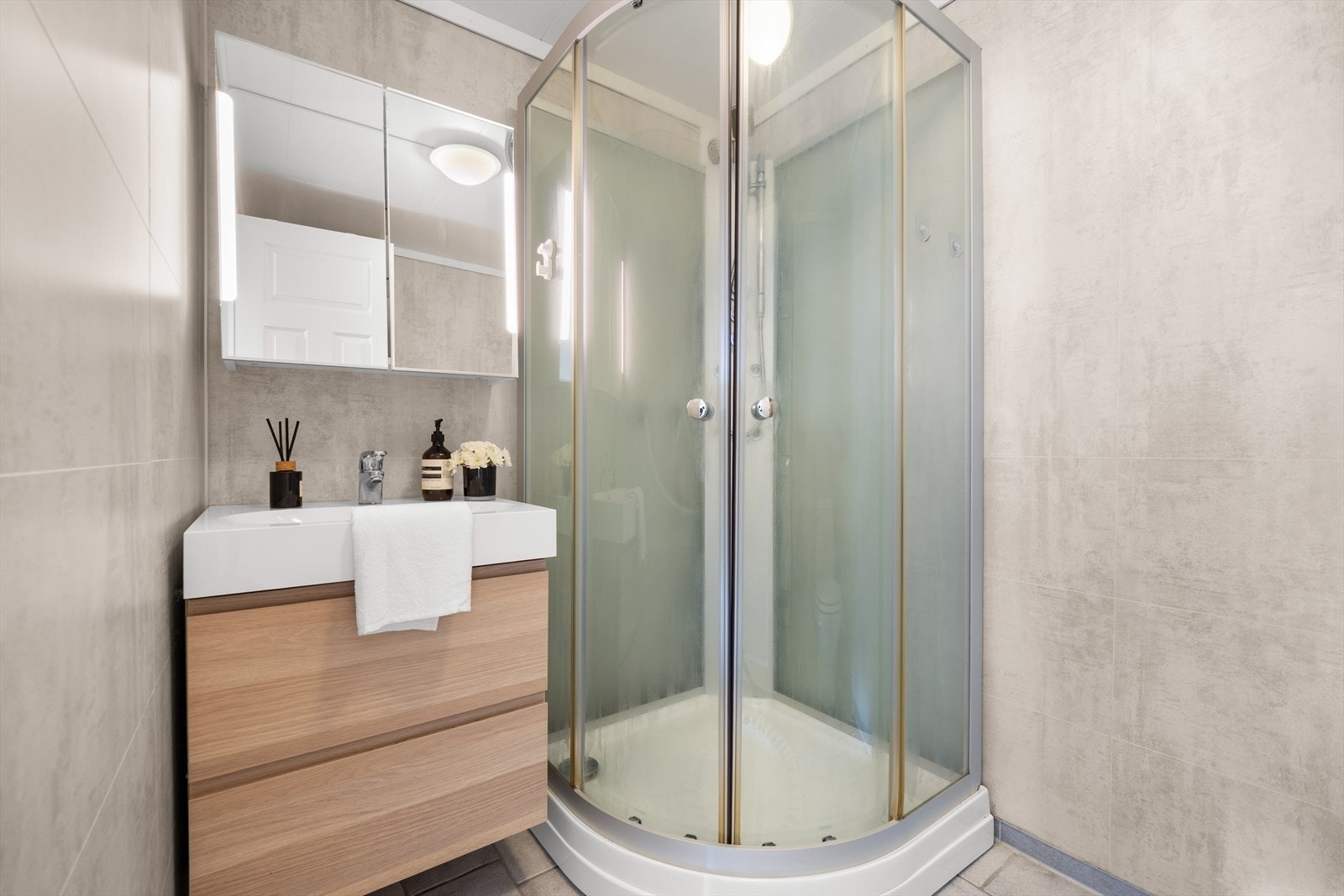 Bad med baderomsplater på vegg og flislagt gulv med varmekabler. Nyere innredning med dusjkabinett, baderomsinnredning og speilskap fra 2016 Galleribilde